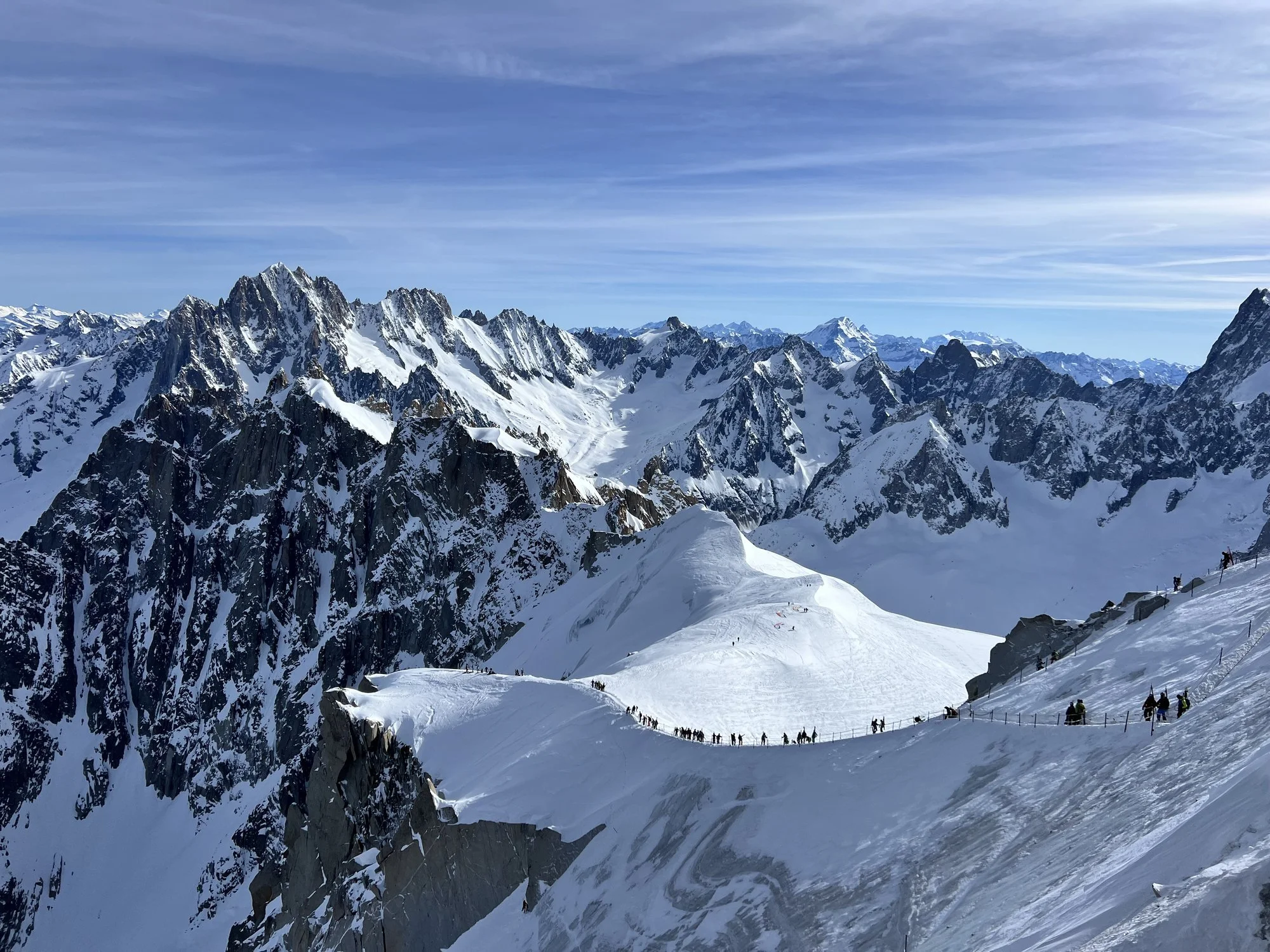 Skiiers walk across a ridge before skiing the Vallée Blanche, surrounded by snowy granite peaks