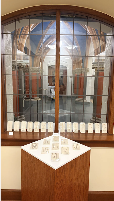 Display with stone artifacts in front of a window showing a historic architectural interior with stone columns and vaulted ceiling.