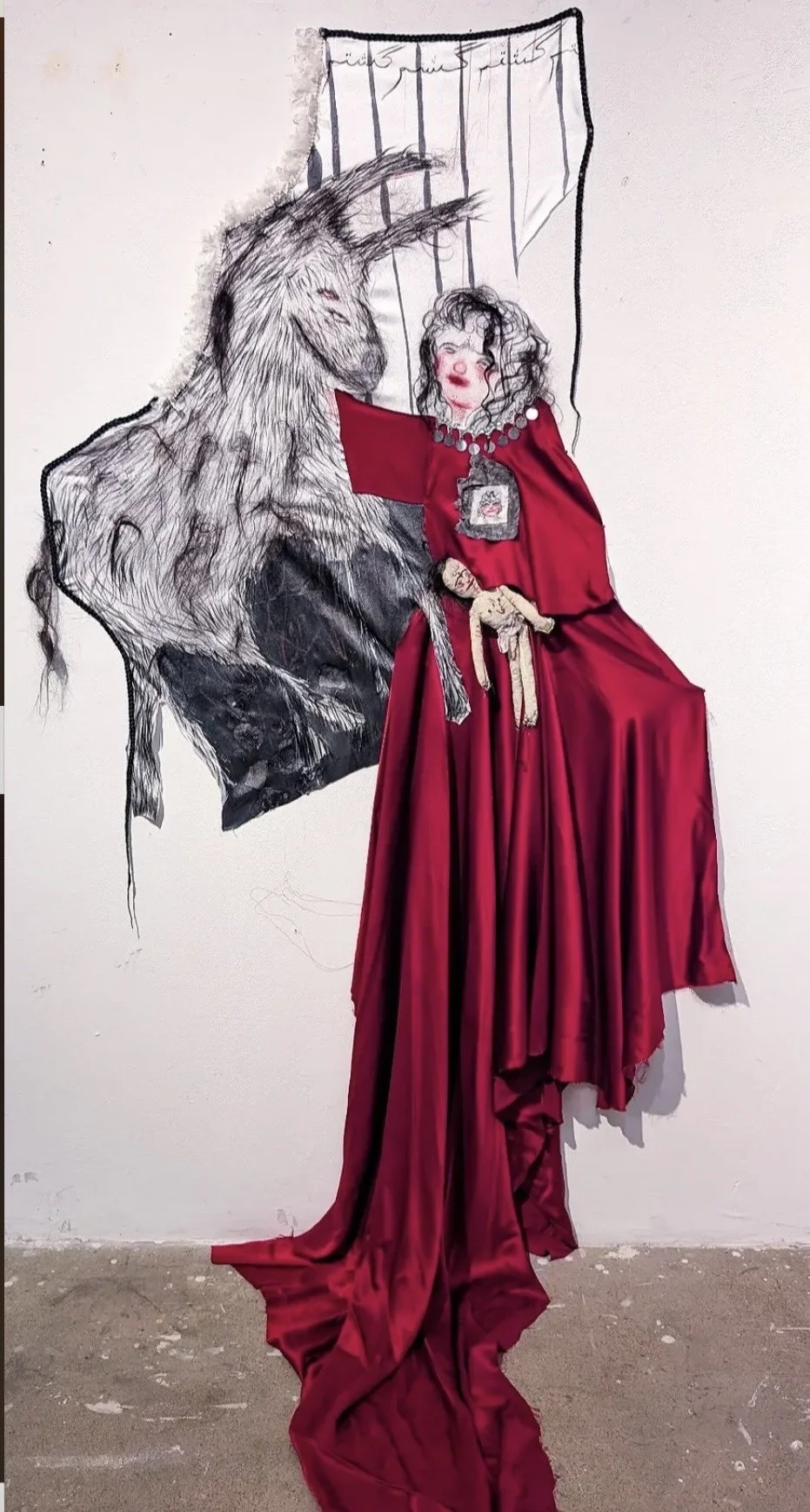 Mixed media artwork featuring a large red velvet dress, partially 3D, with a sketch of a woman with curly hair and a wolf behind her in black ink on the wall.