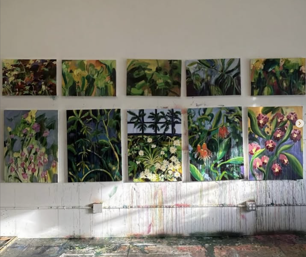 A series of ten colorful abstract landscape paintings hung on a white wall in an art studio. The paintings depict various scenes of nature with plants, trees, flowers, and lush greenery.