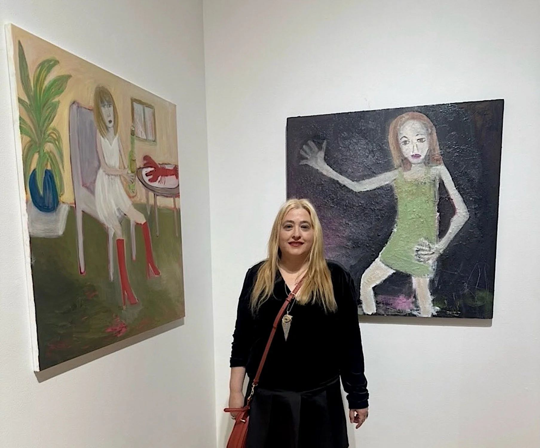 A woman with blonde hair and a black outfit standing in an art gallery, with two paintings on the white wall behind her. The painting on the left depicts a woman sitting at a table with a potted plant and bookshelf, using abstract style with emphasized red and green colors. The painting on the right shows a woman with red hair in a green dress with an arm raised, painted in a textured, expressive style.