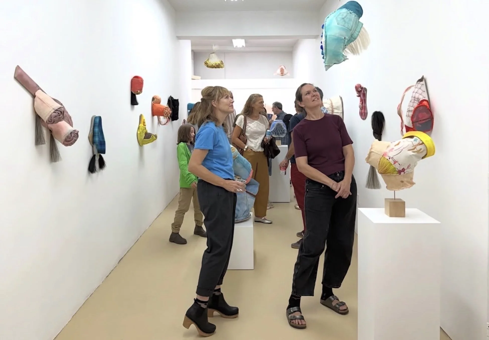 Visitors observing textile art sculptures on display wall in an art gallery.