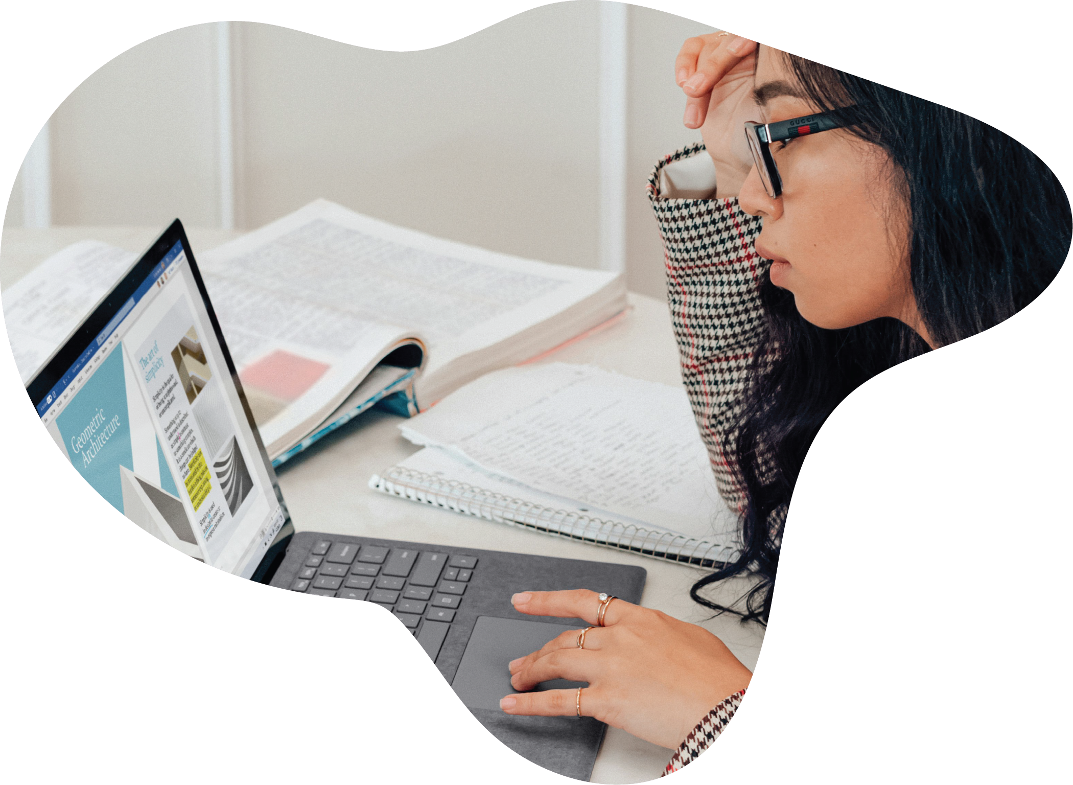 Designer working on a laptop with notes, books, and project materials.
