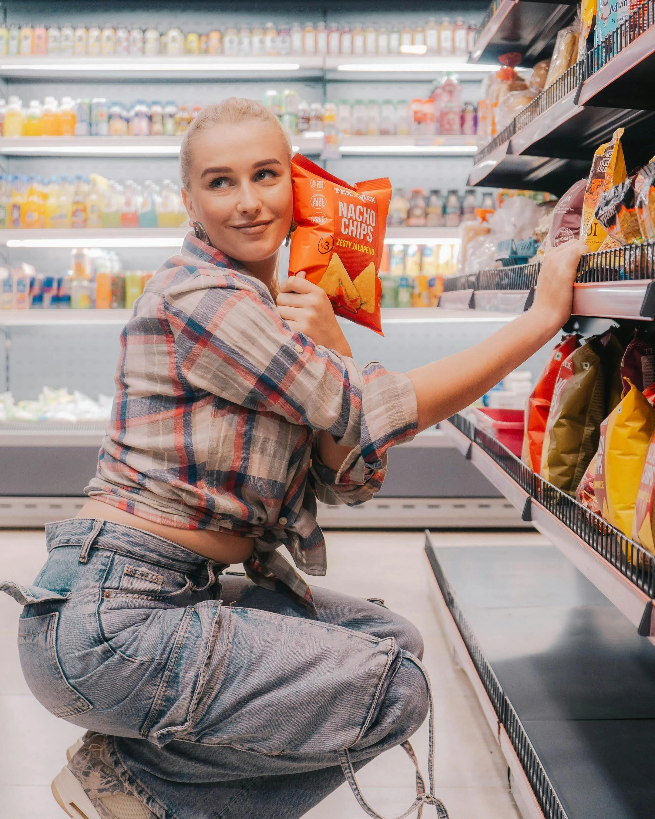 A young woman is grocery shopping and holds a bag of chips