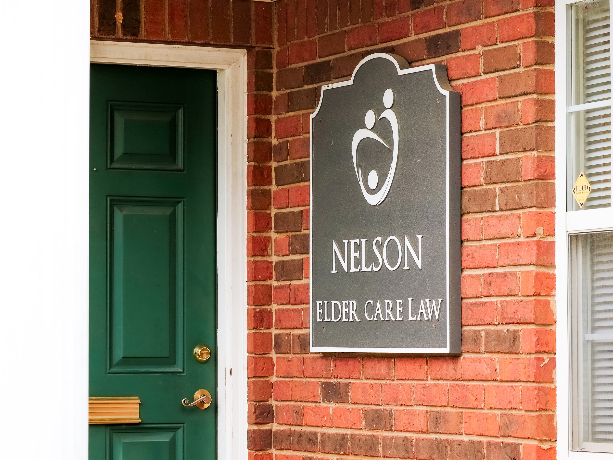 Sign reading 'Nelson Elder Care Law' next to a green door on a red brick wall.