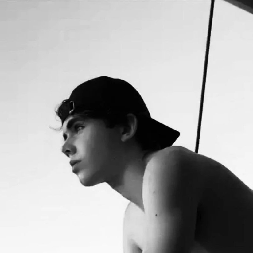 A young man wearing a backwards cap, looking to the side, in black and white.