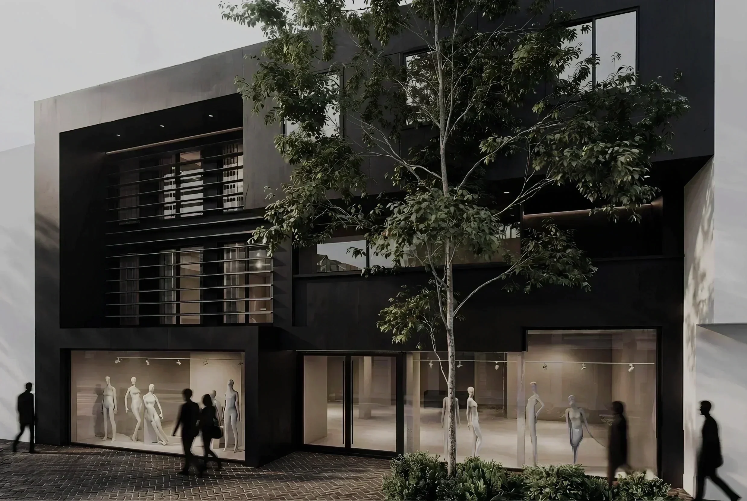 Night view of a modern building with mannequins displayed in windows and a tree outside.