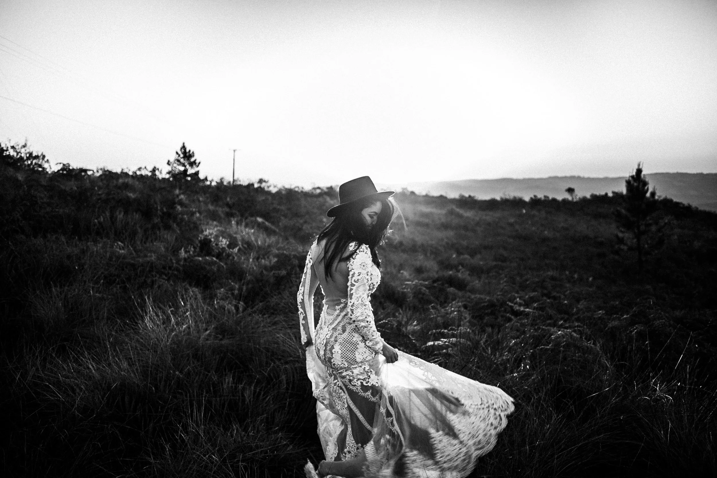Black and white photo of a woman in a white lace dress and hat in a field.