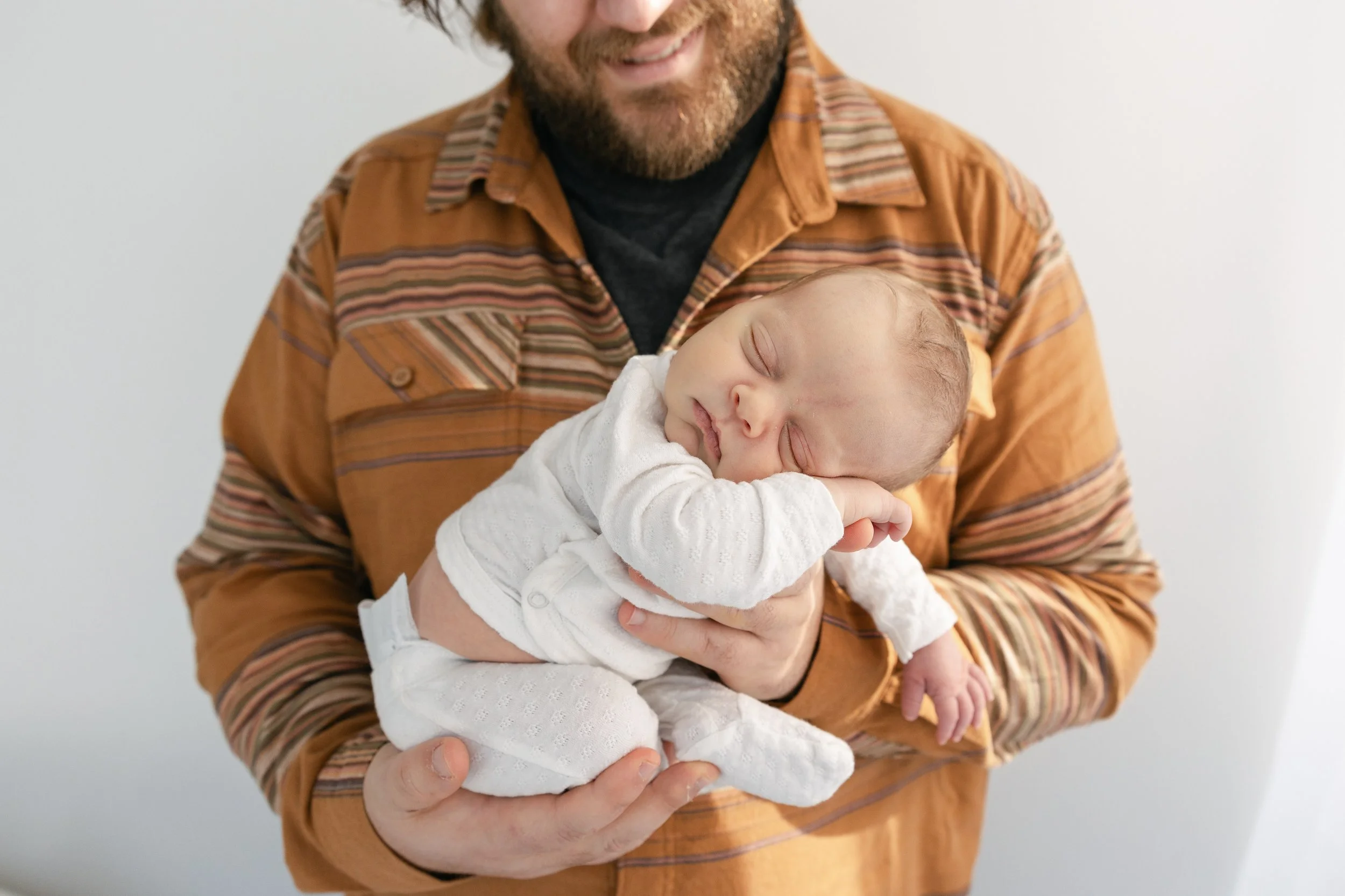 A man holding a sleeping baby with one hand supporting the baby's chest and the other hand under the baby's knees, both smiling.