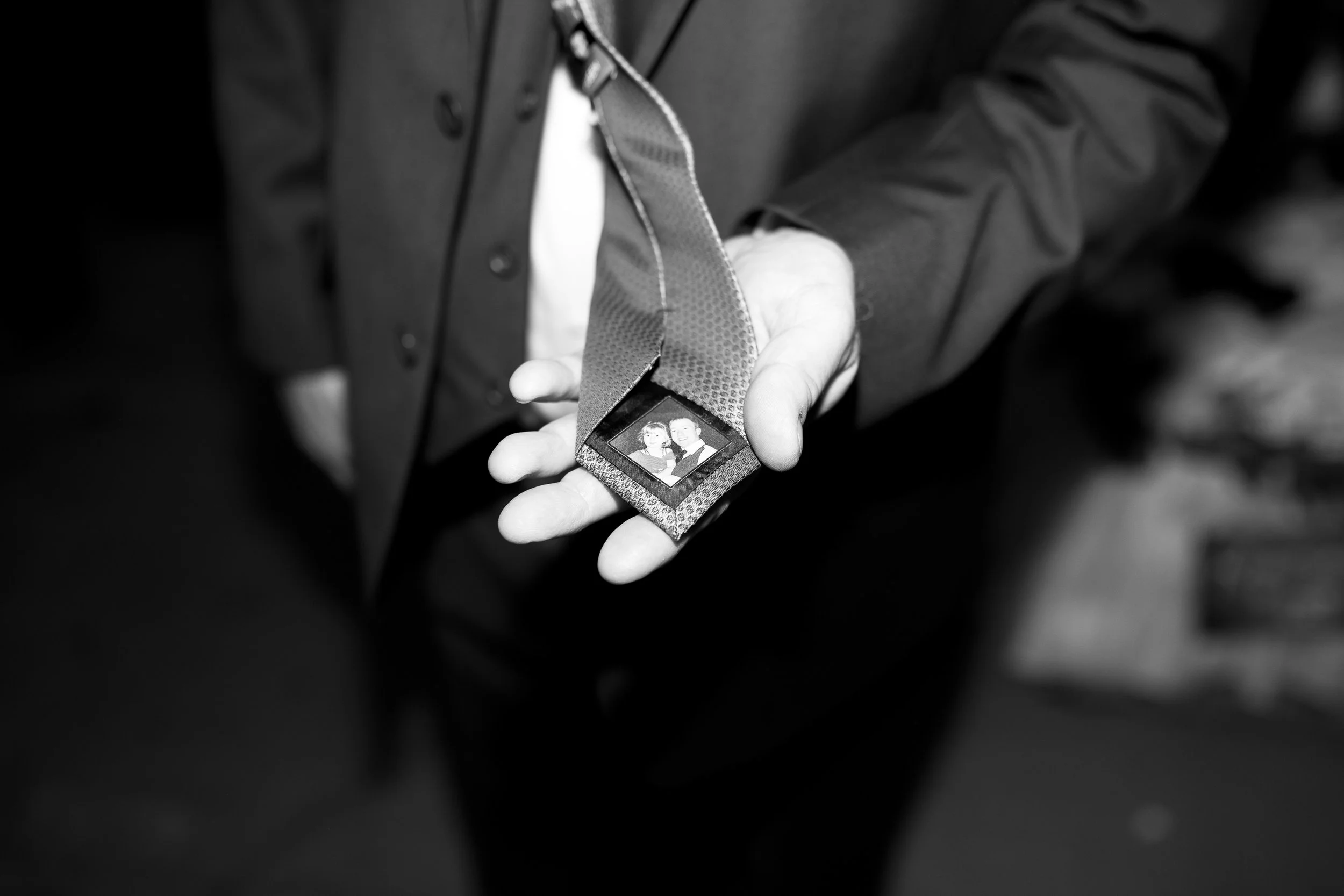 A person's hand holding a lanyard with a photo ID badge attached, showing two people in formal attire, possibly at a special event or ceremony.