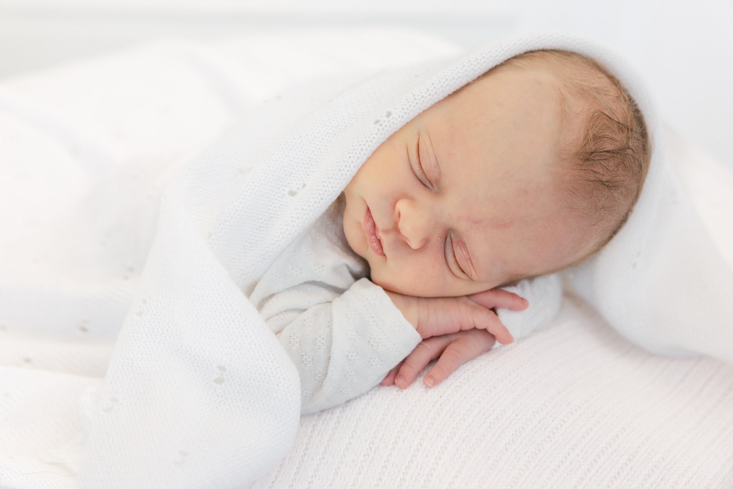 A sleeping baby wrapped in a white blanket, resting on a soft white surface.