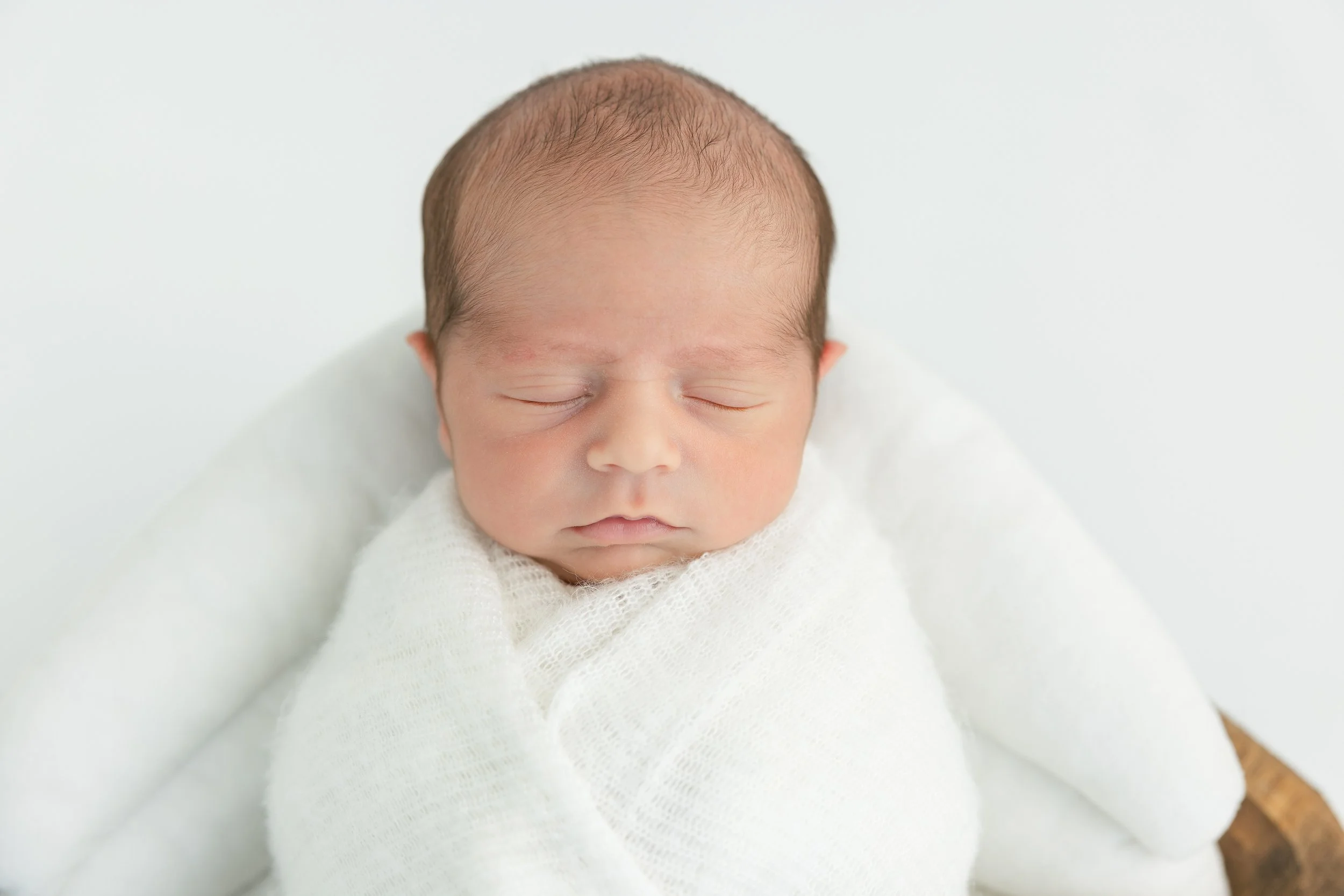 A sleeping newborn baby wrapped in a white blanket, resting on a soft surface.
