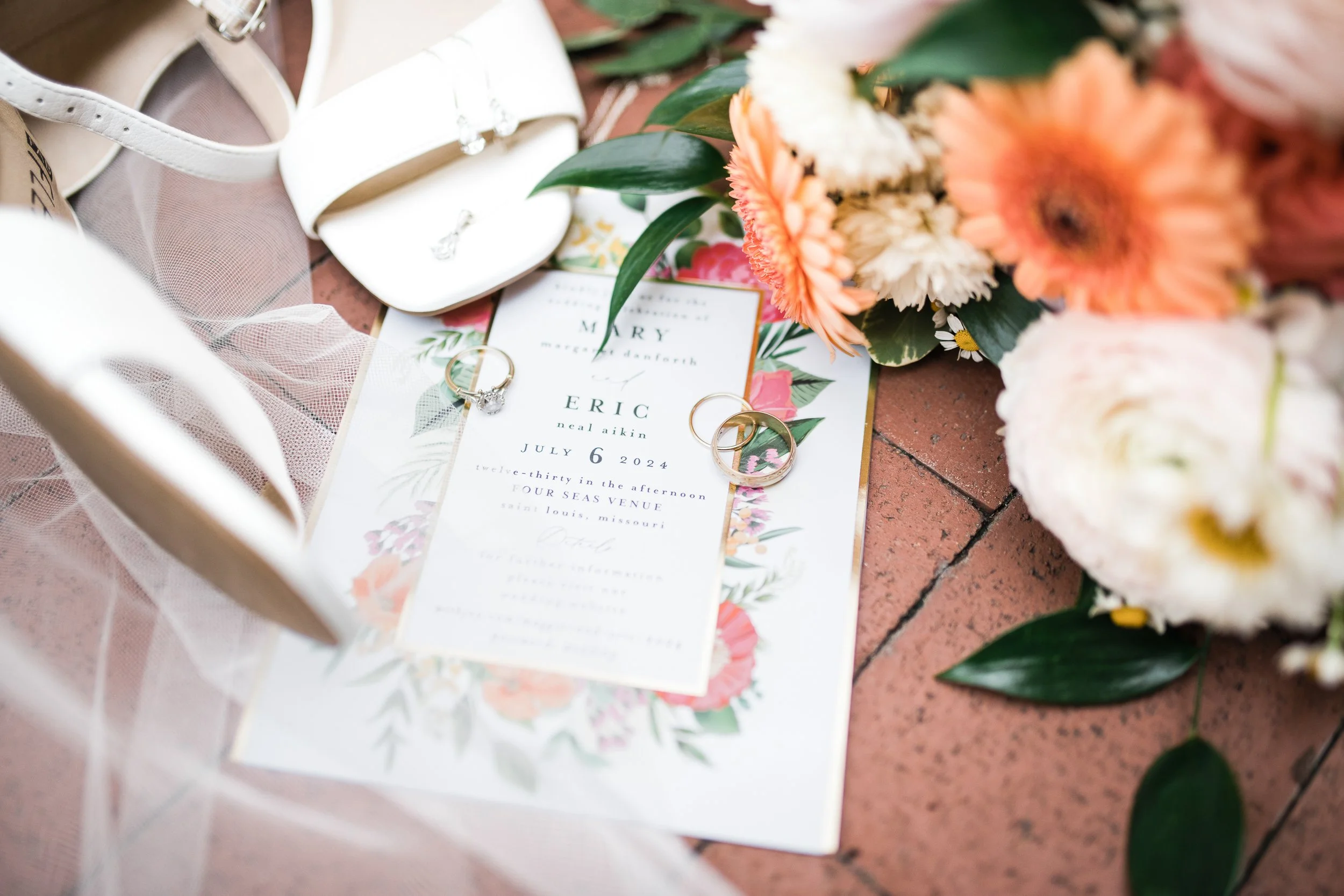 Wedding invitation with flowers, rings, and a white purse on a brick surface