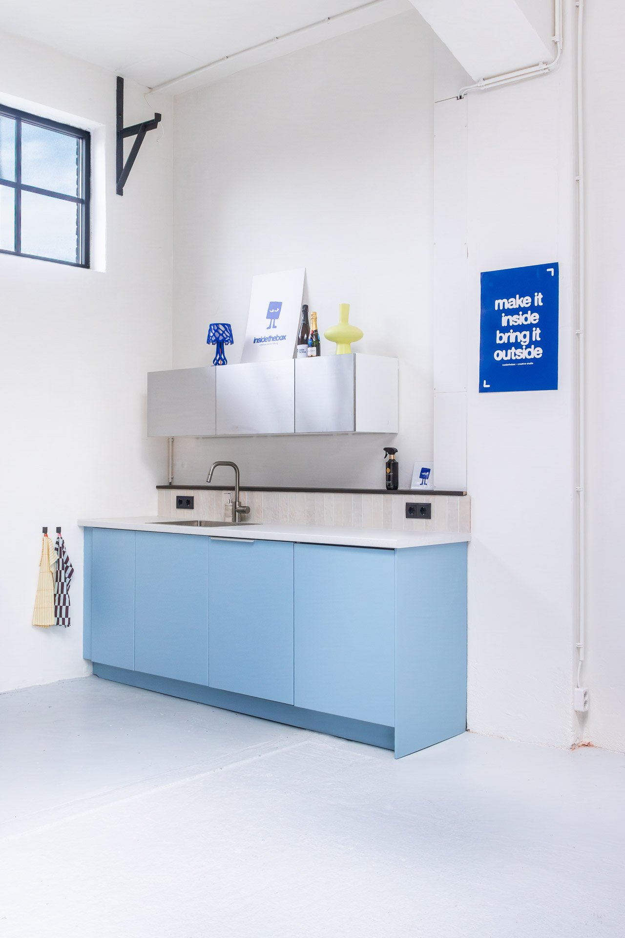 Interieurfotografie van een industriële studioruimte met een op maat gemaakte blauwe keuken, hoge witte wanden en een strakke visuele compositie.