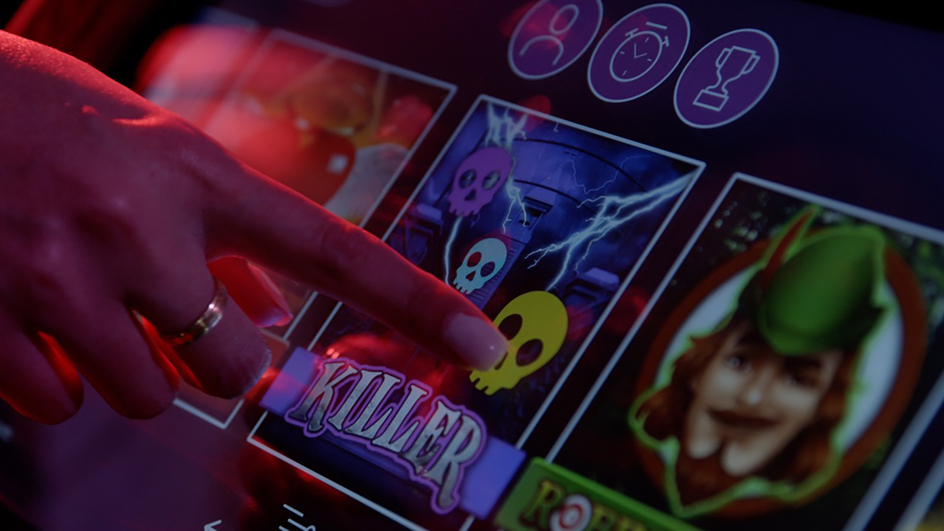 Close-up of a finger touching a touchscreen with casino game icons and the word "Killer" displayed.