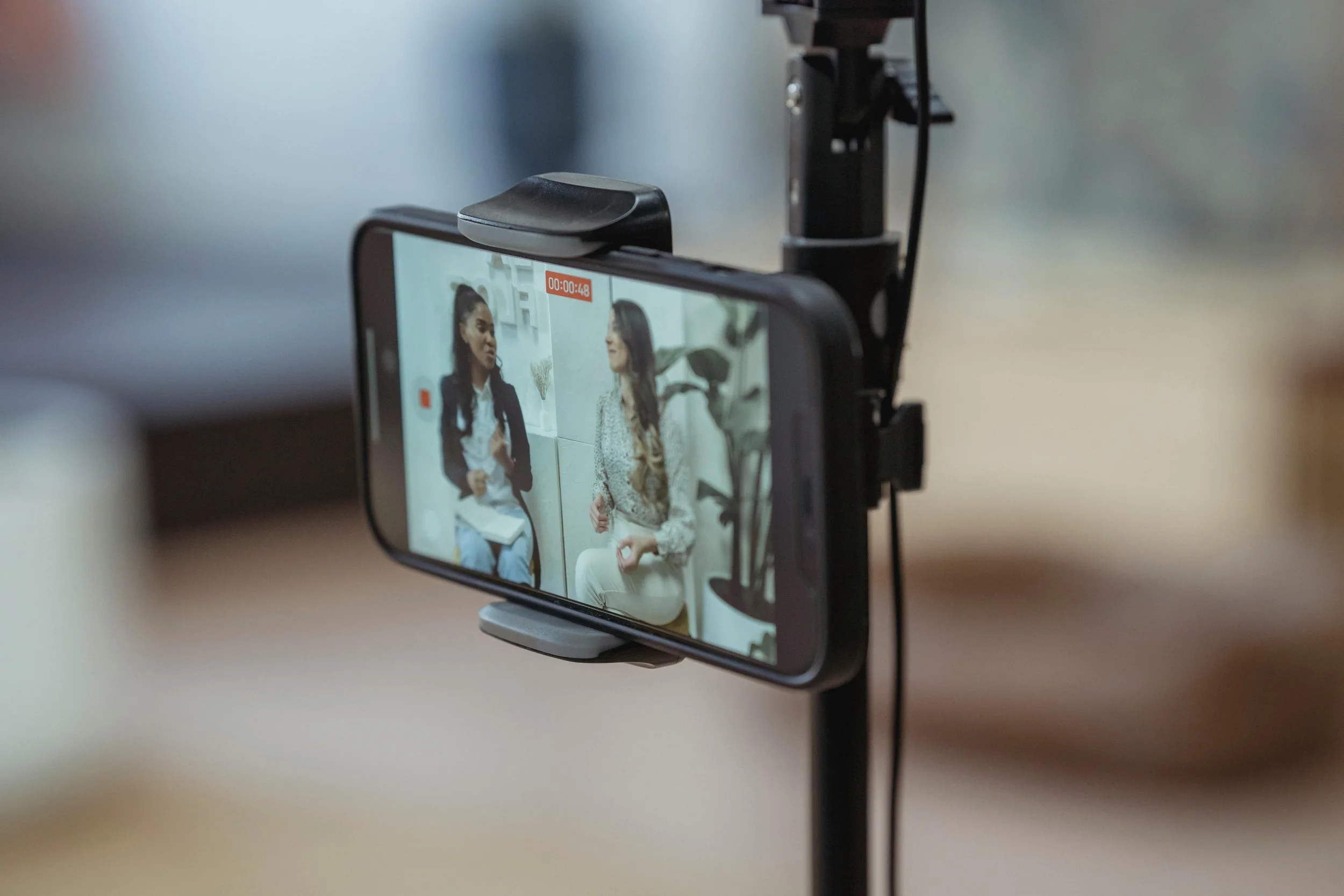 Smartphone on a stand recording two women engaged in conversation indoors.