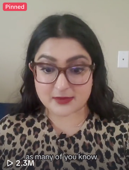 Woman with dark hair, glasses, and leopard print top, sitting against a beige wall with a white light switch.