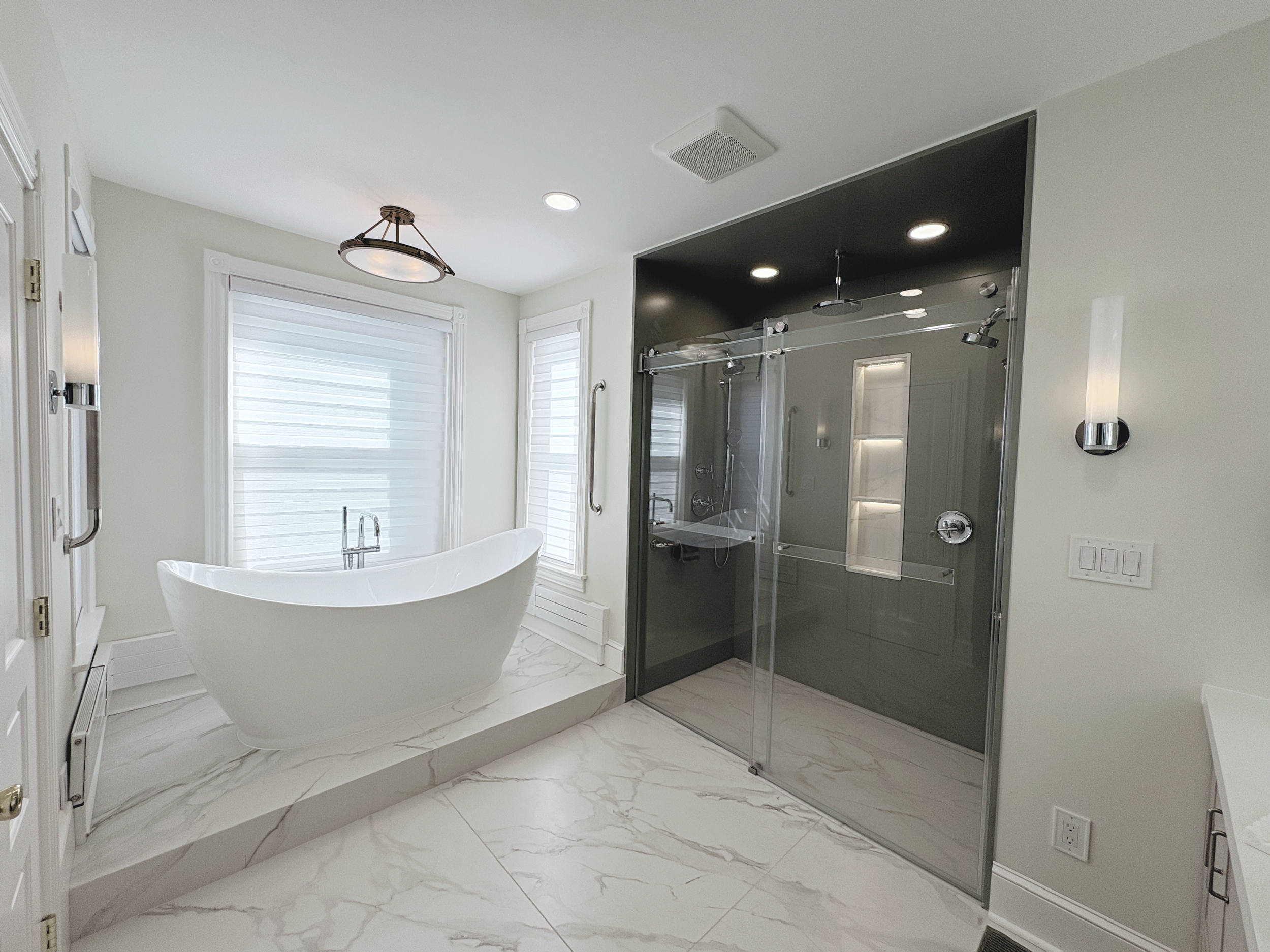 A modern bathroom featuring a white freestanding bathtub, large windows with white blinds, a walk-in shower with glass doors, and marble floor tiles.