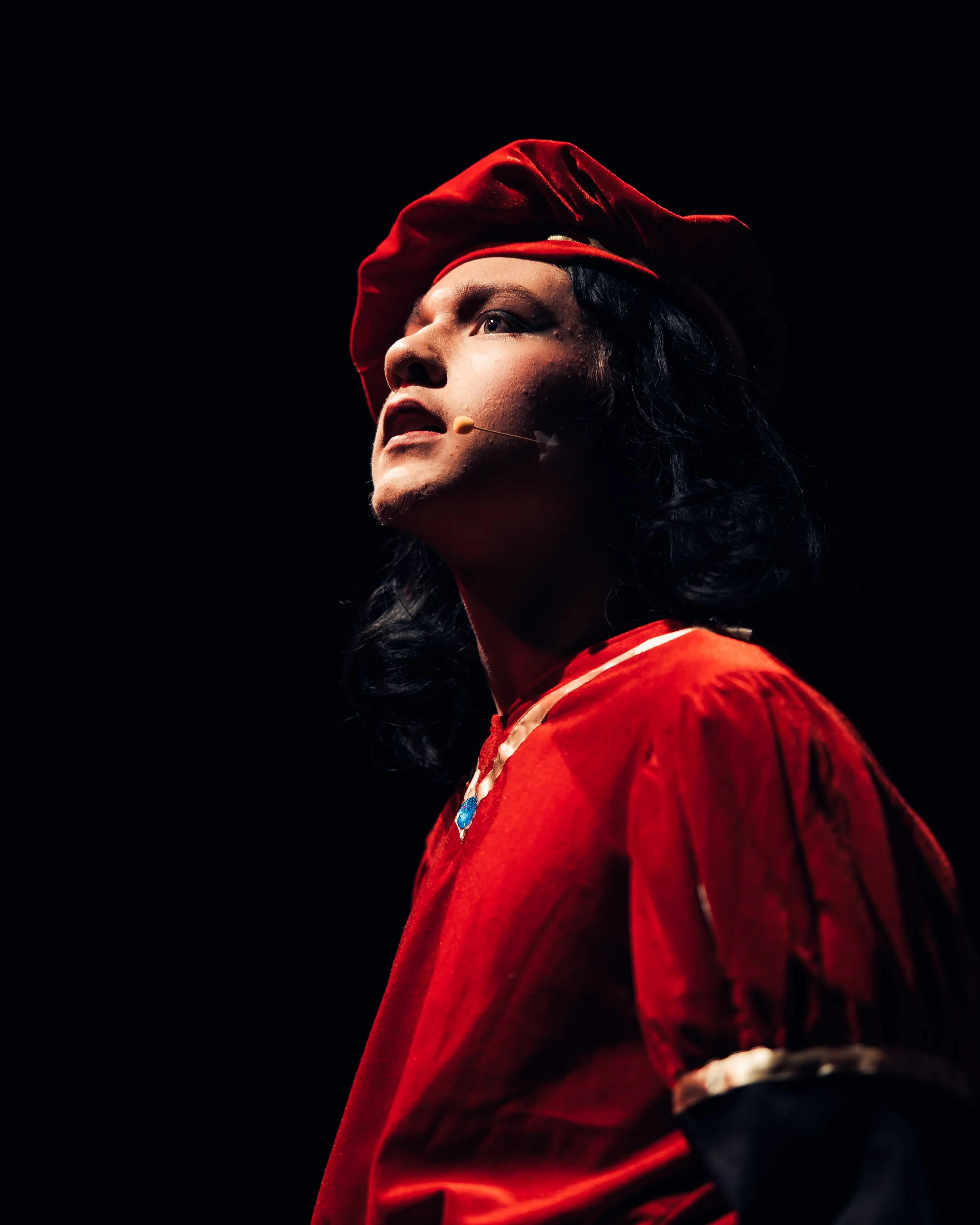 Performer in a red Renaissance costume and headset microphone looking up.