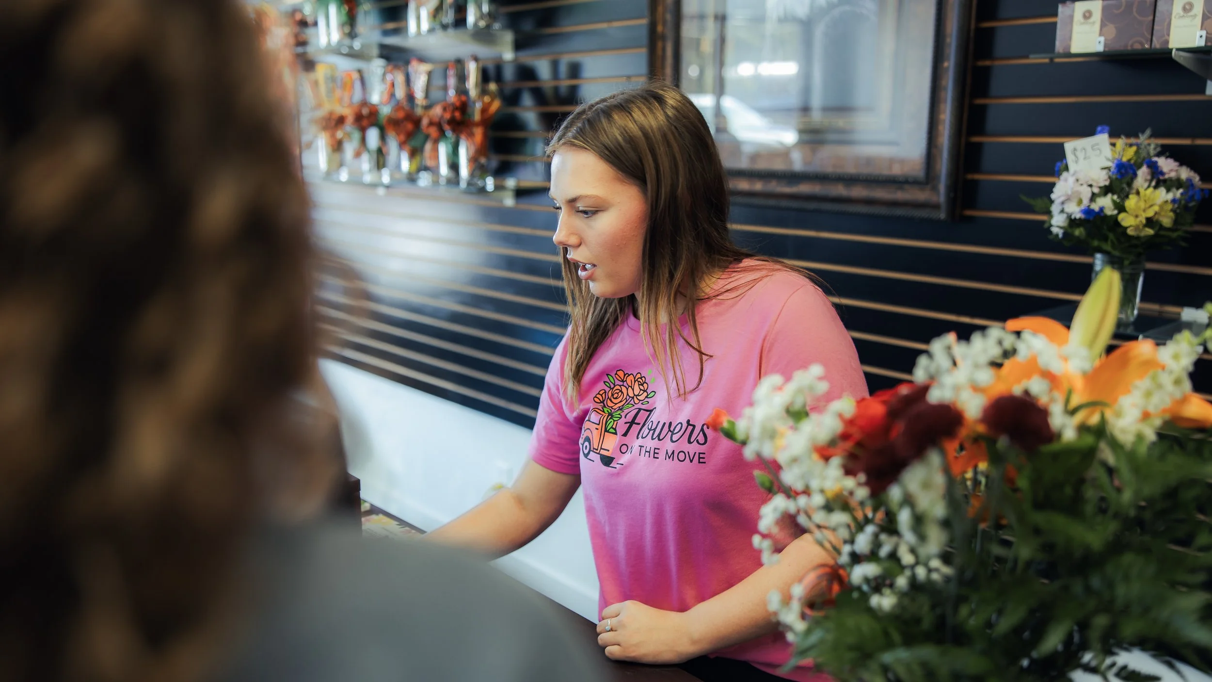 A Flowers on the Move employee speaks with a customer beside a floral arrangement.