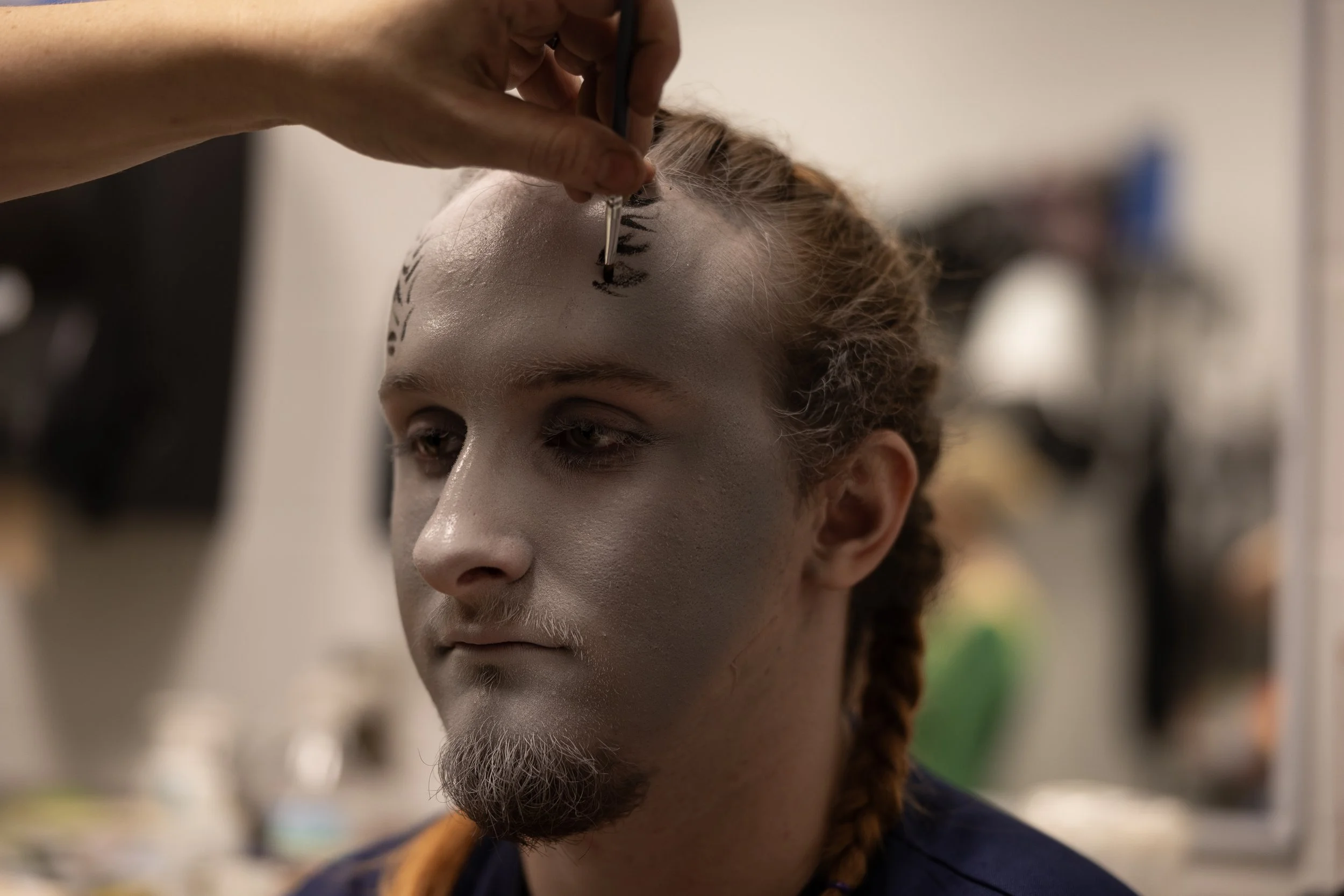 A cast member sits still while makeup is applied to their forehead.