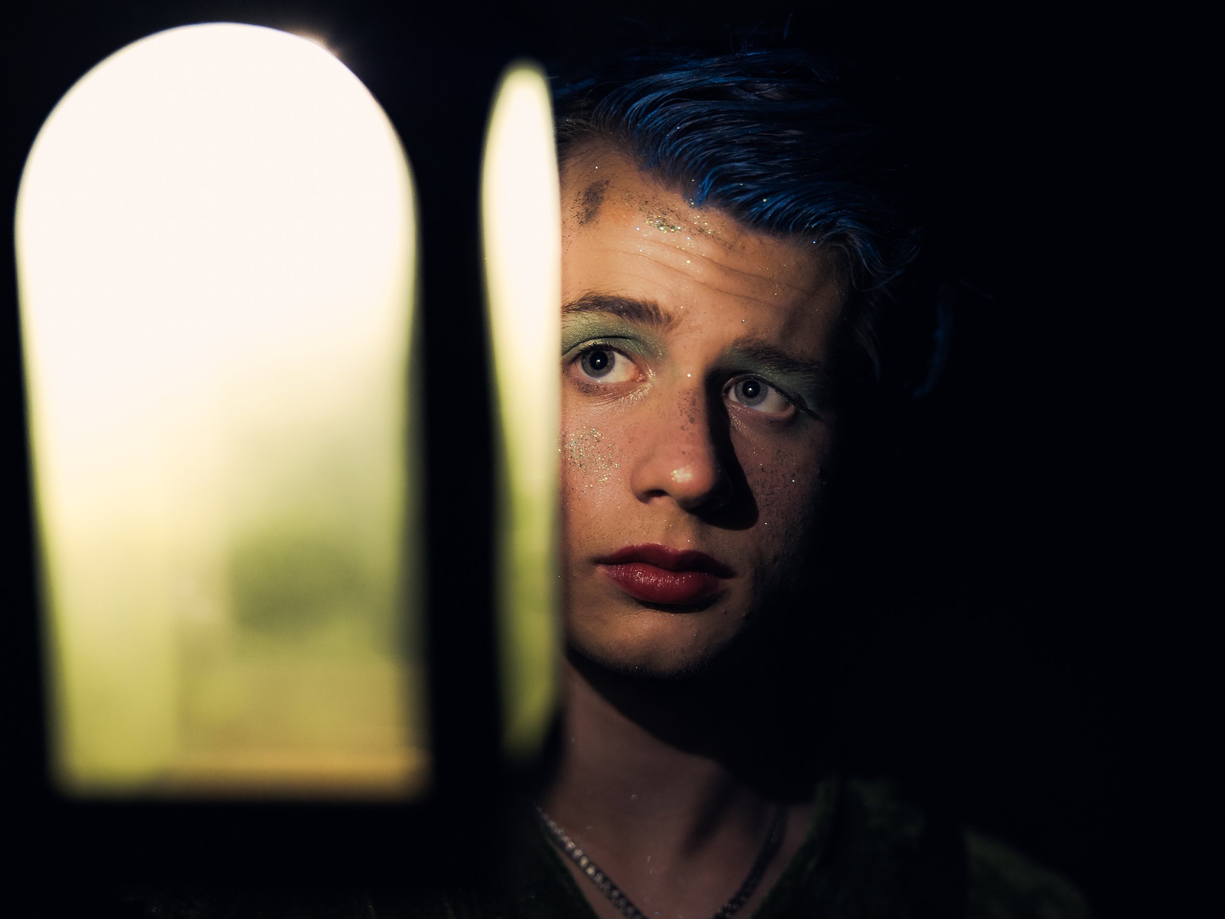 Close view of Peter Pan in glitter stage makeup and a lantern against dark green velvet.