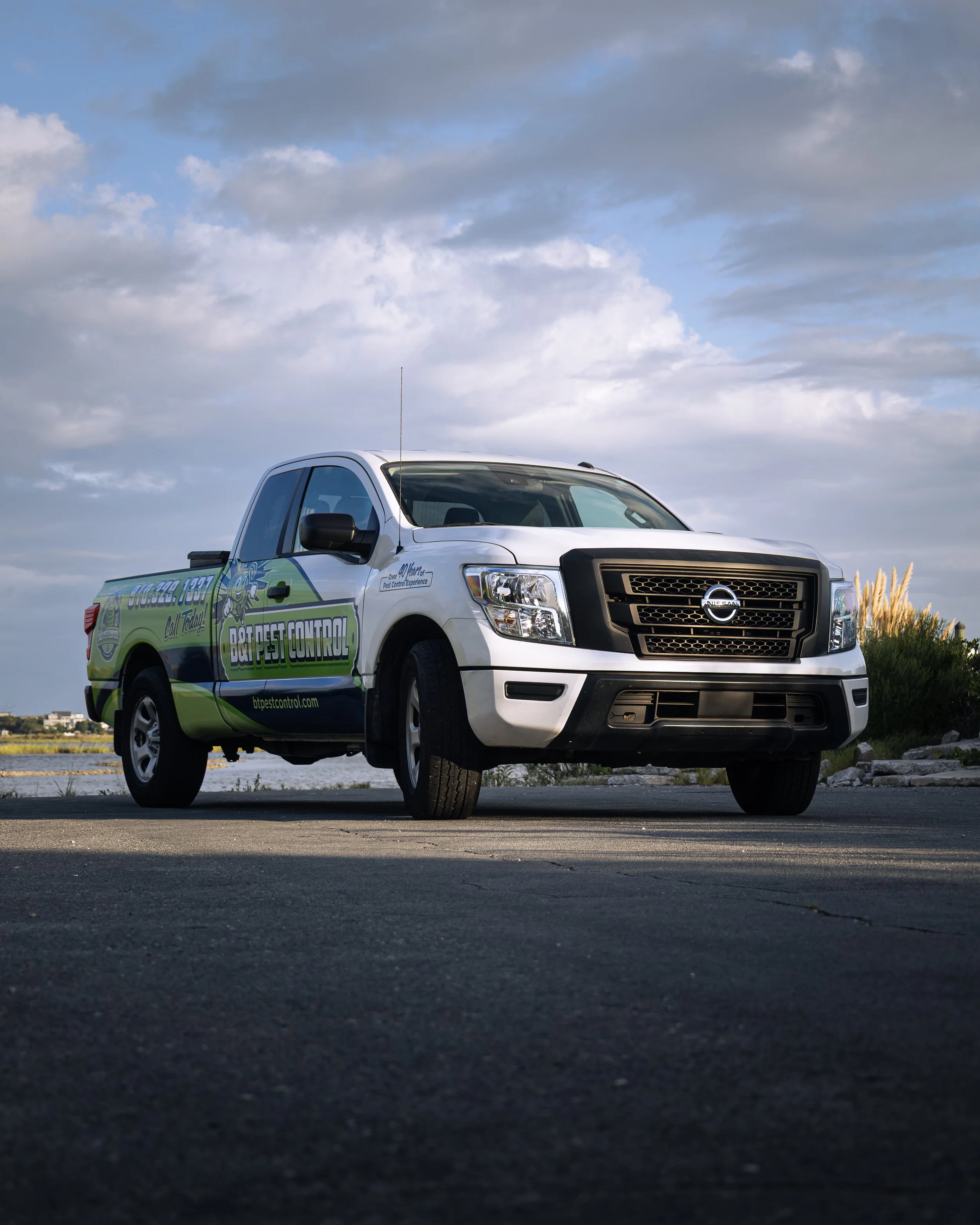 A B&T Pest Control pickup with green branding beneath a cloud-filled sky.