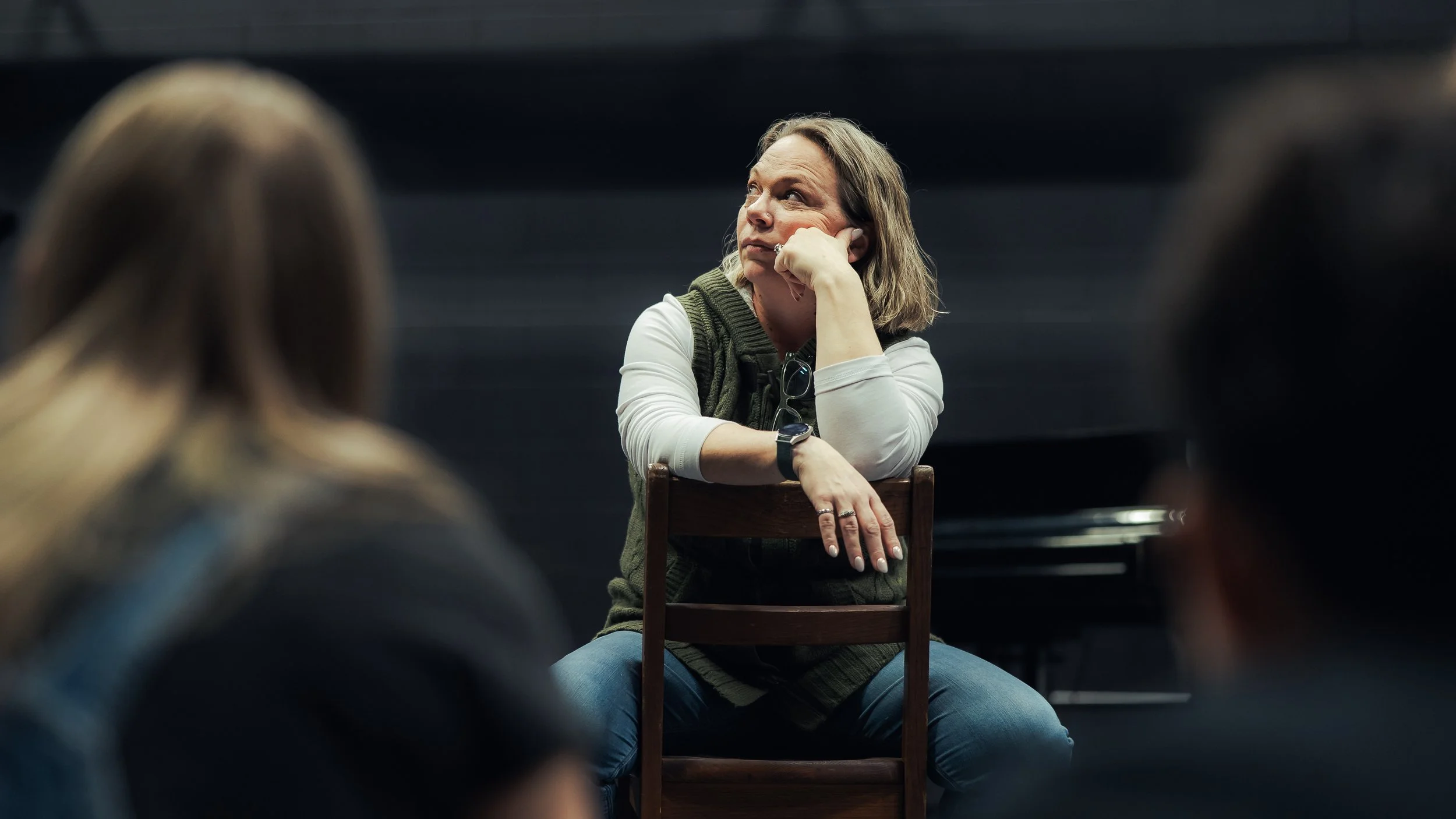 A seated rehearsal moment in the auditorium, with other cast members in the foreground.