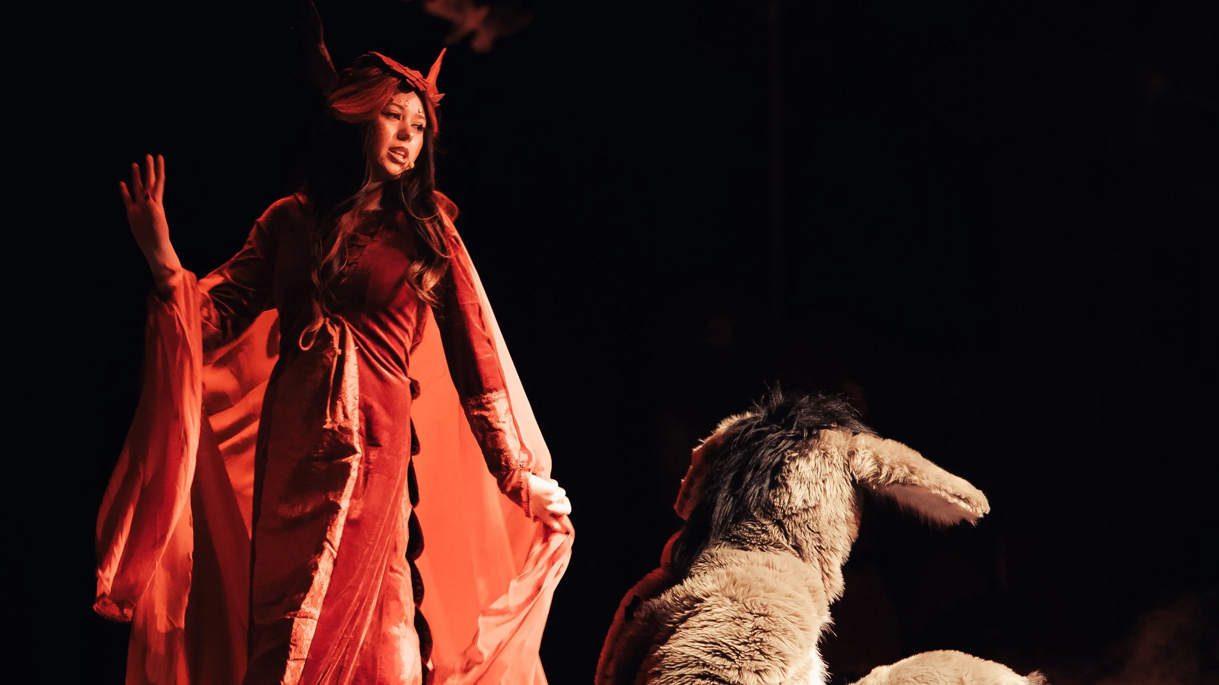 Dragon in a red costume sings toward Donkey on a dark stage during Shrek the Musical.