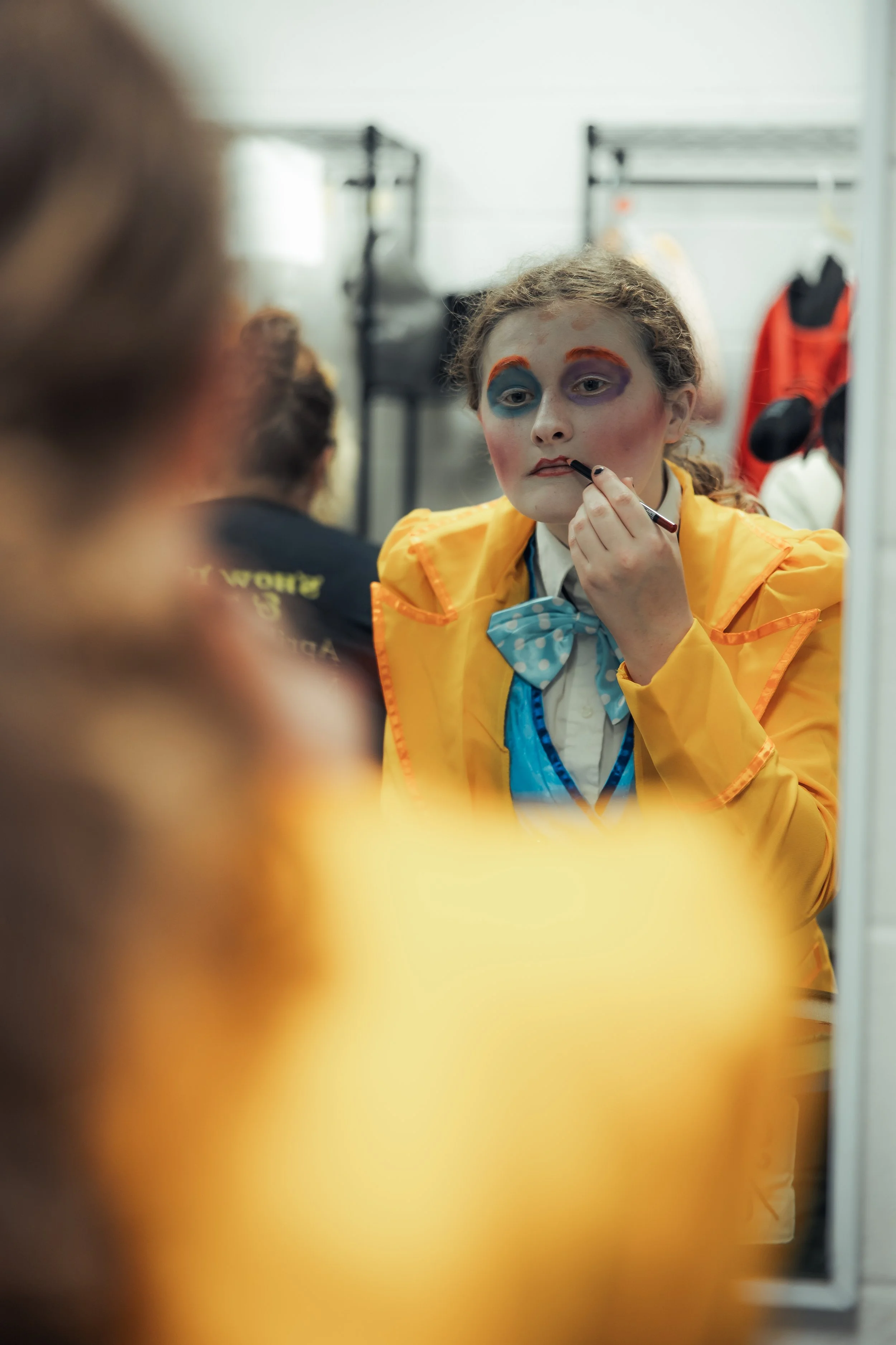 A performer checks their makeup in a dressing-room mirror.