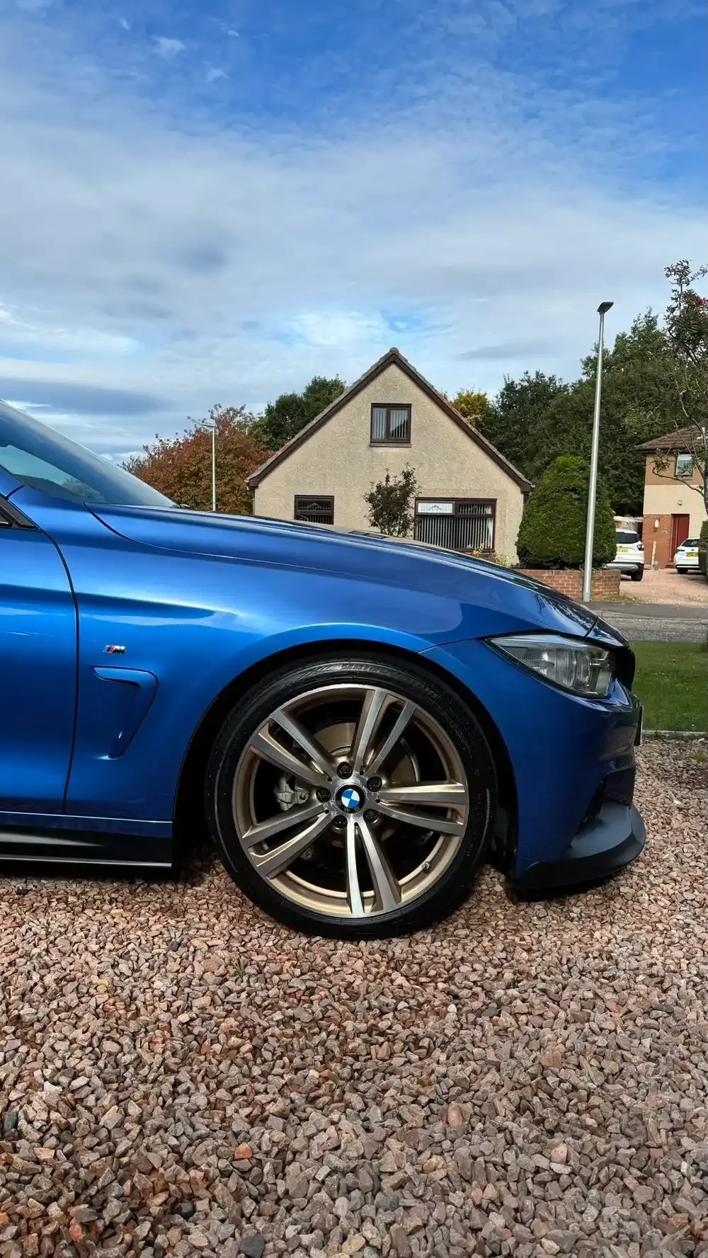 Blue BMW M3 parked on a gravel driveway in front of a house with a front yard.