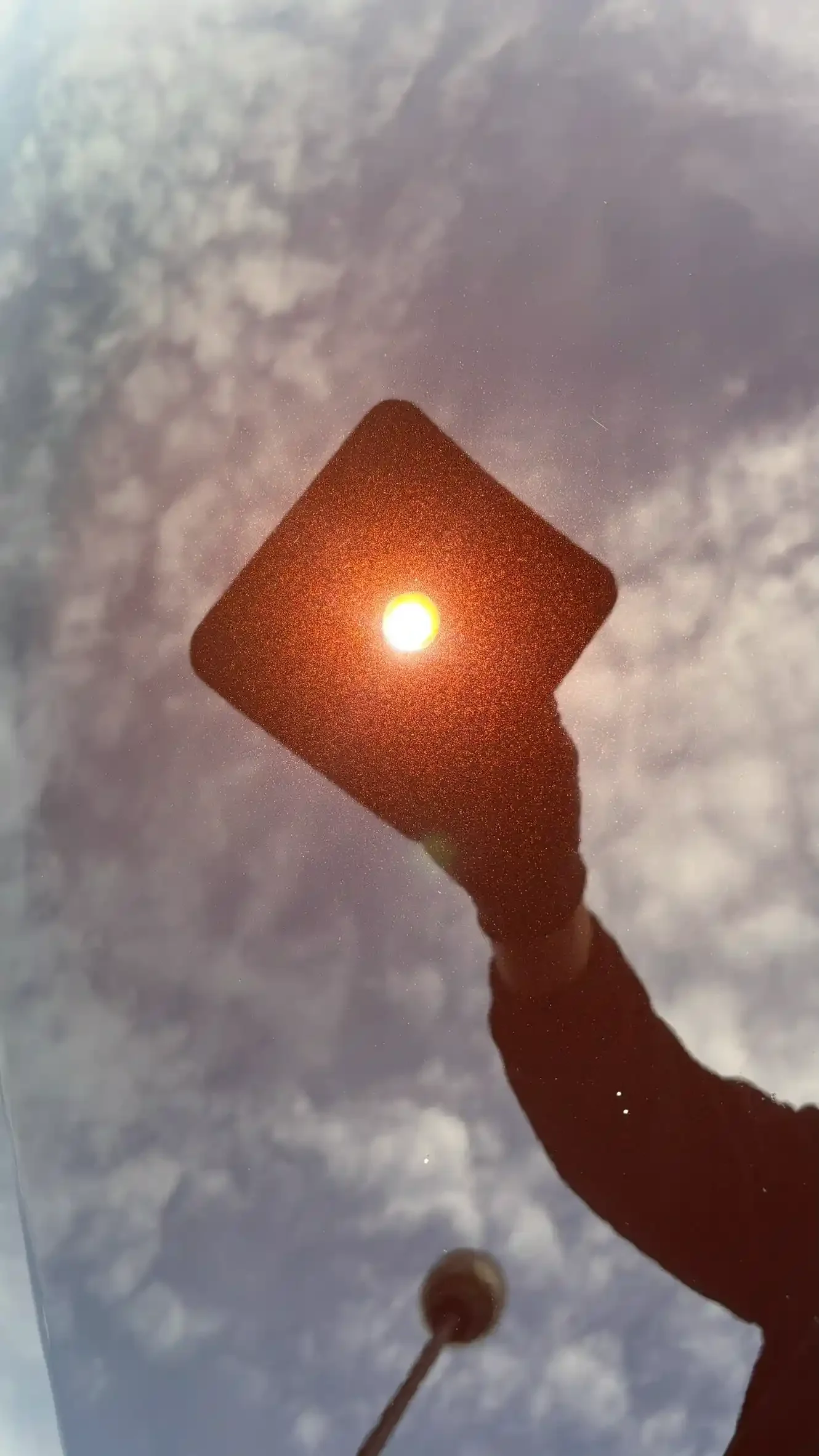 Person holding a sign with a circular light behind it, against a cloudy sky.