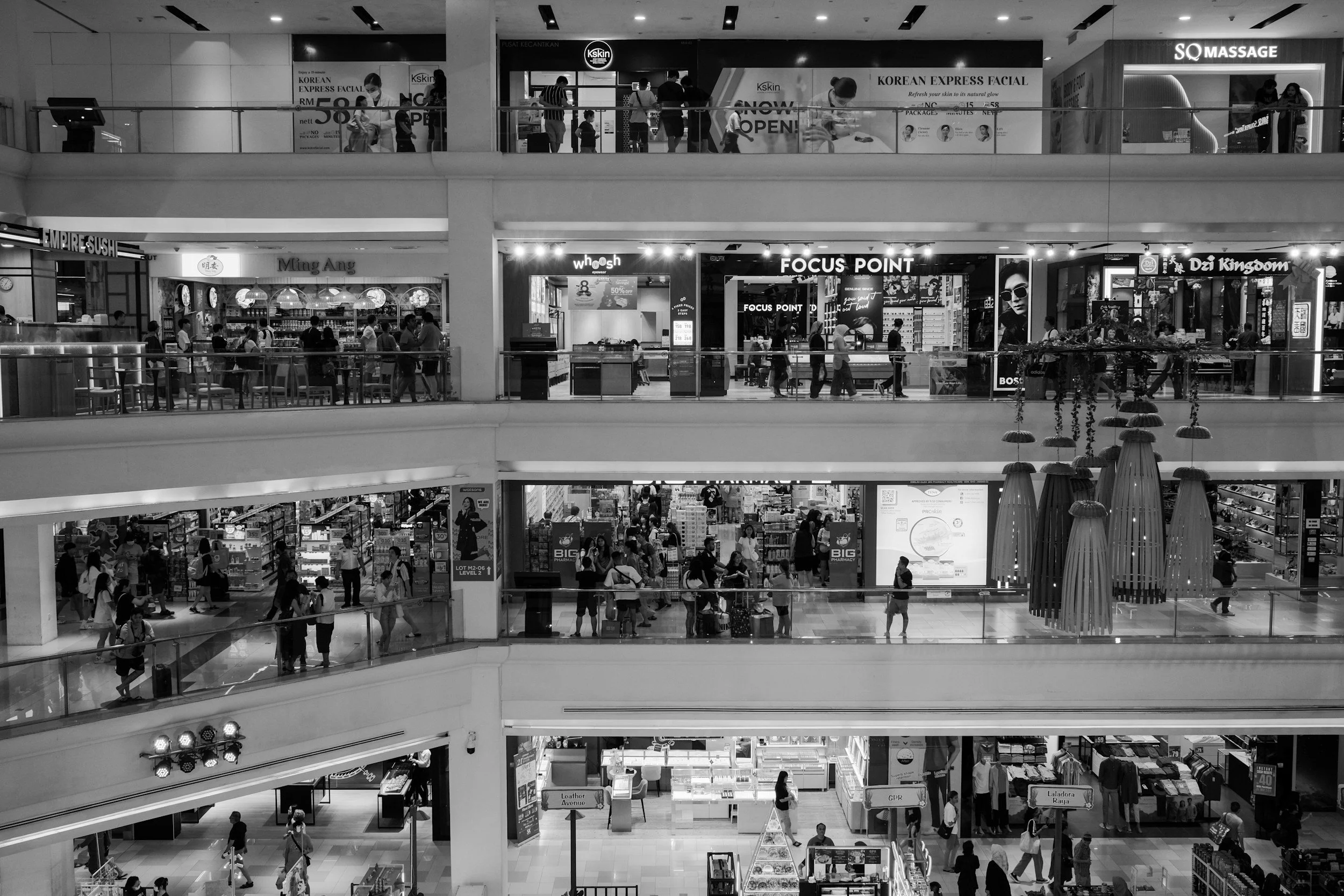 Multiple floors inside a shopping mall with various retail stores, eateries, and many shoppers walking and browsing.