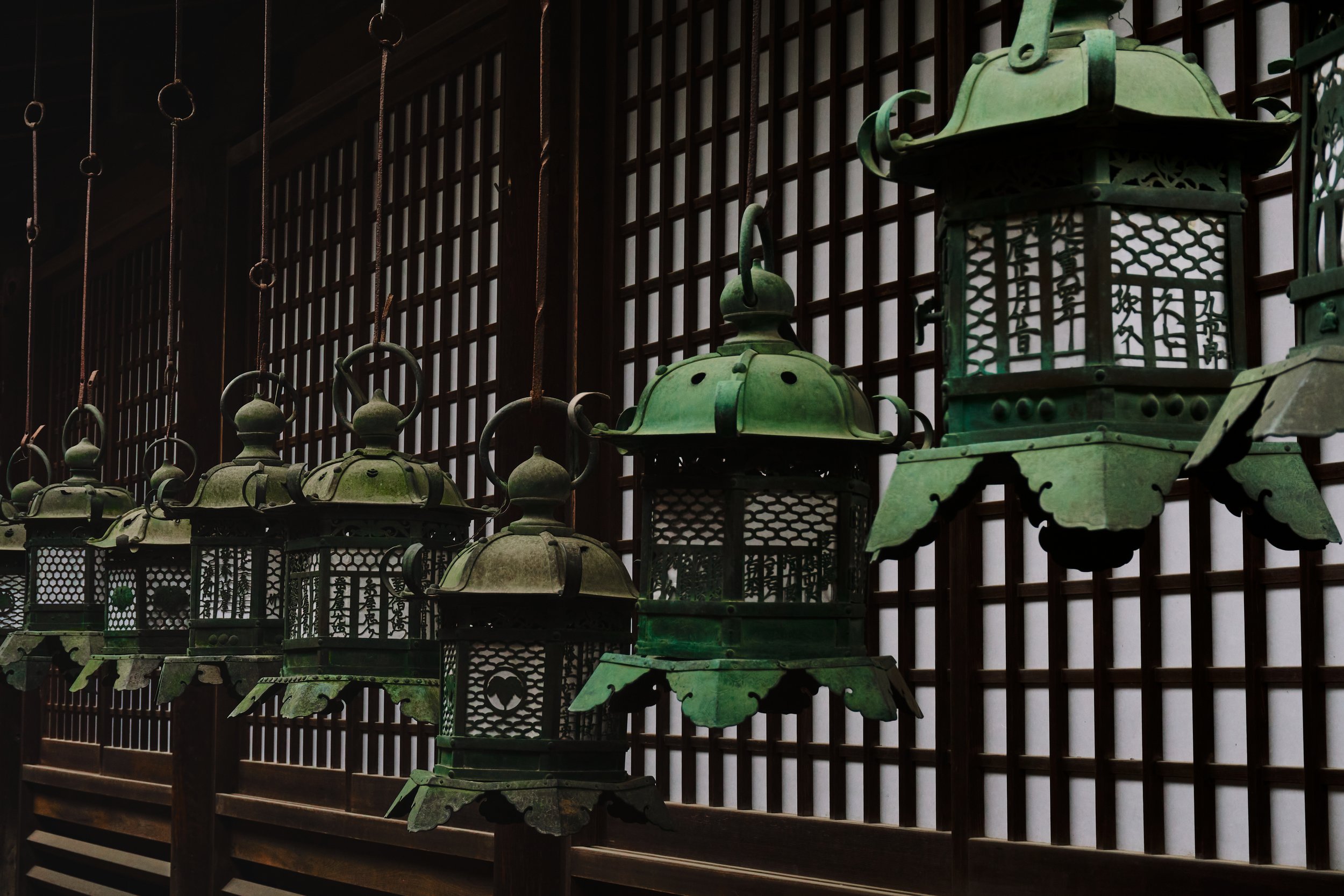 Row of green traditional Japanese lanterns hanging in front of wooden lattice windows.