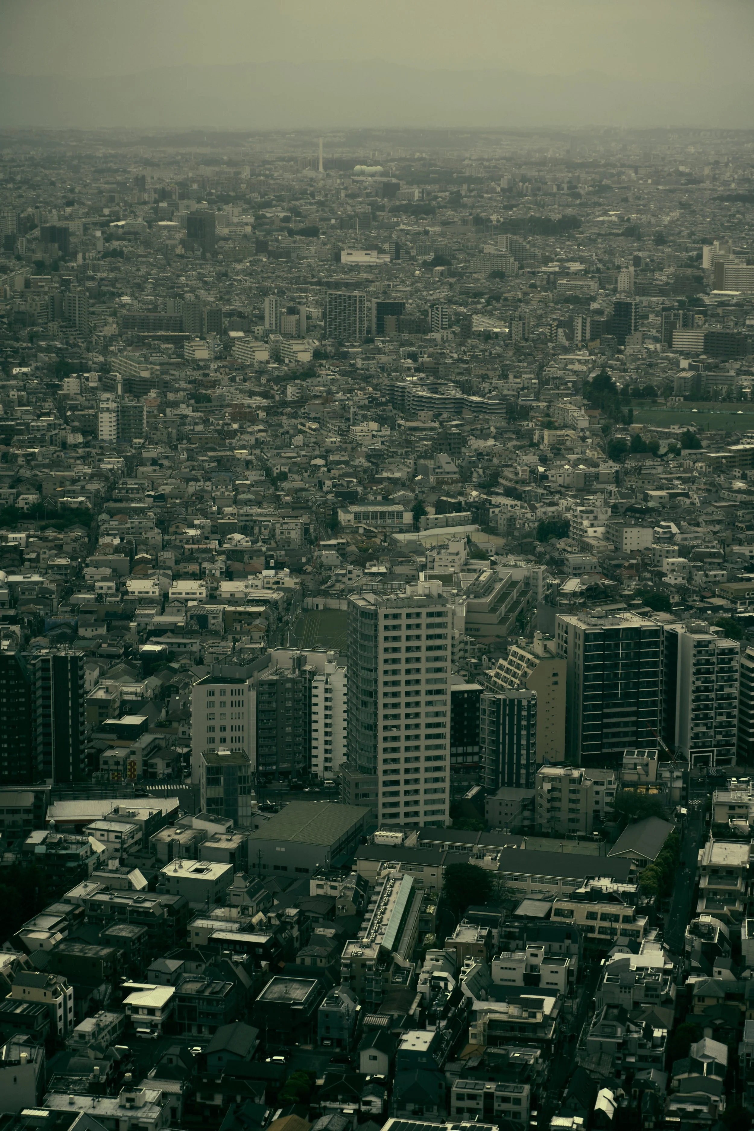 Aerial view of a large cityscape with numerous buildings and skyscrapers under overcast skies.
