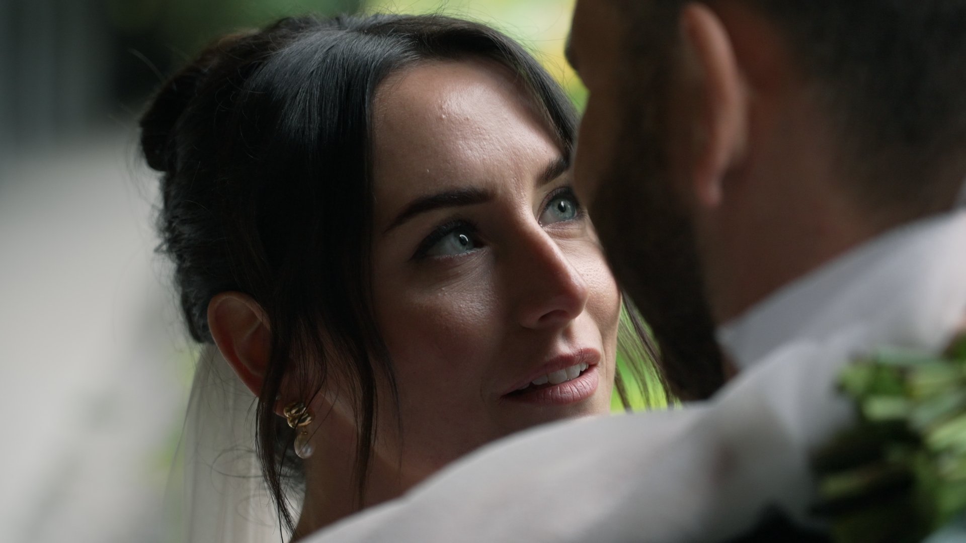 Close-up of a woman with dark hair and blue eyes looking into a man's face in an intimate moment. wedding photo