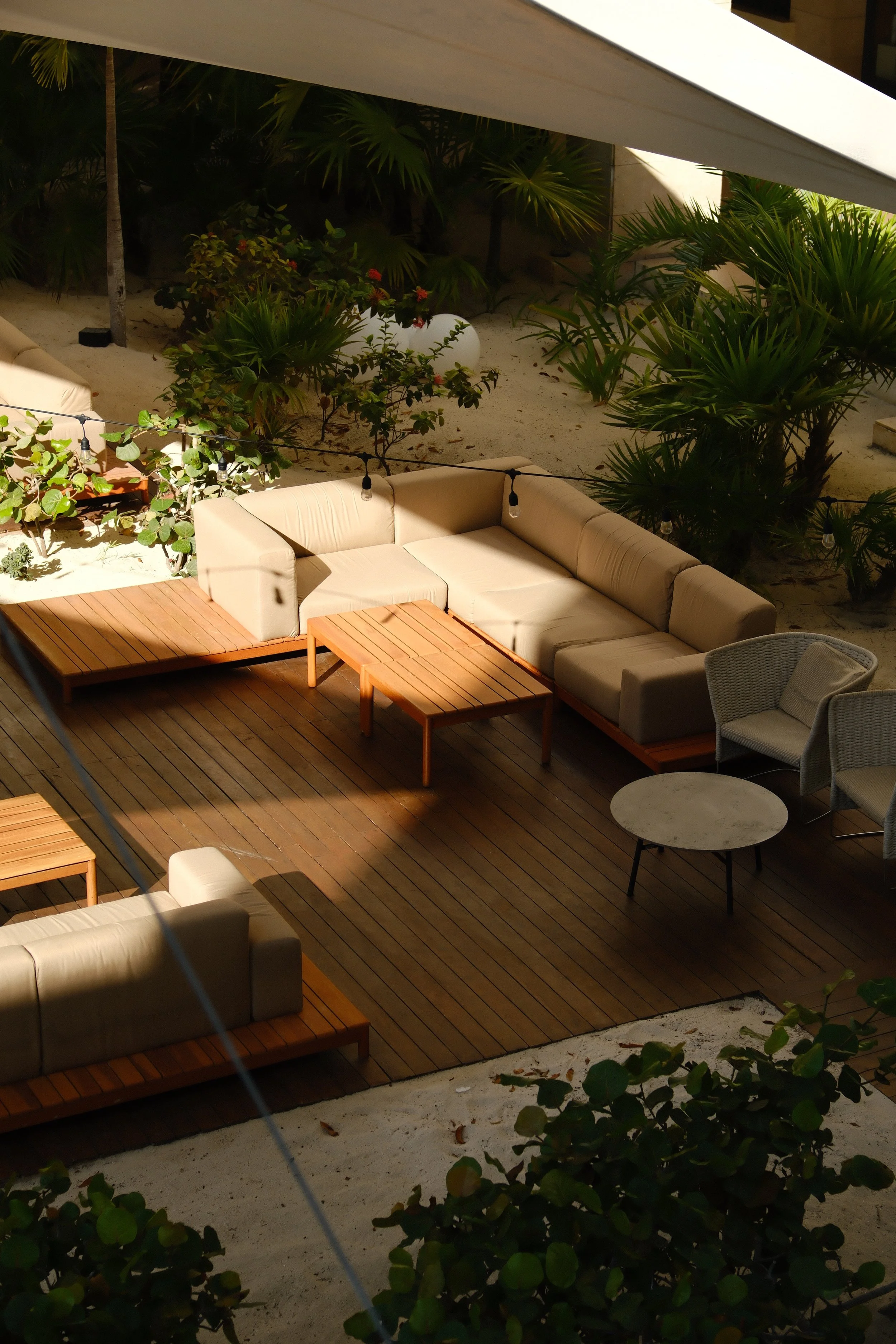 Modern office lounge area with beige sofa, yellow chairs around a small round table, and large windows showing high-rise buildings outside.
