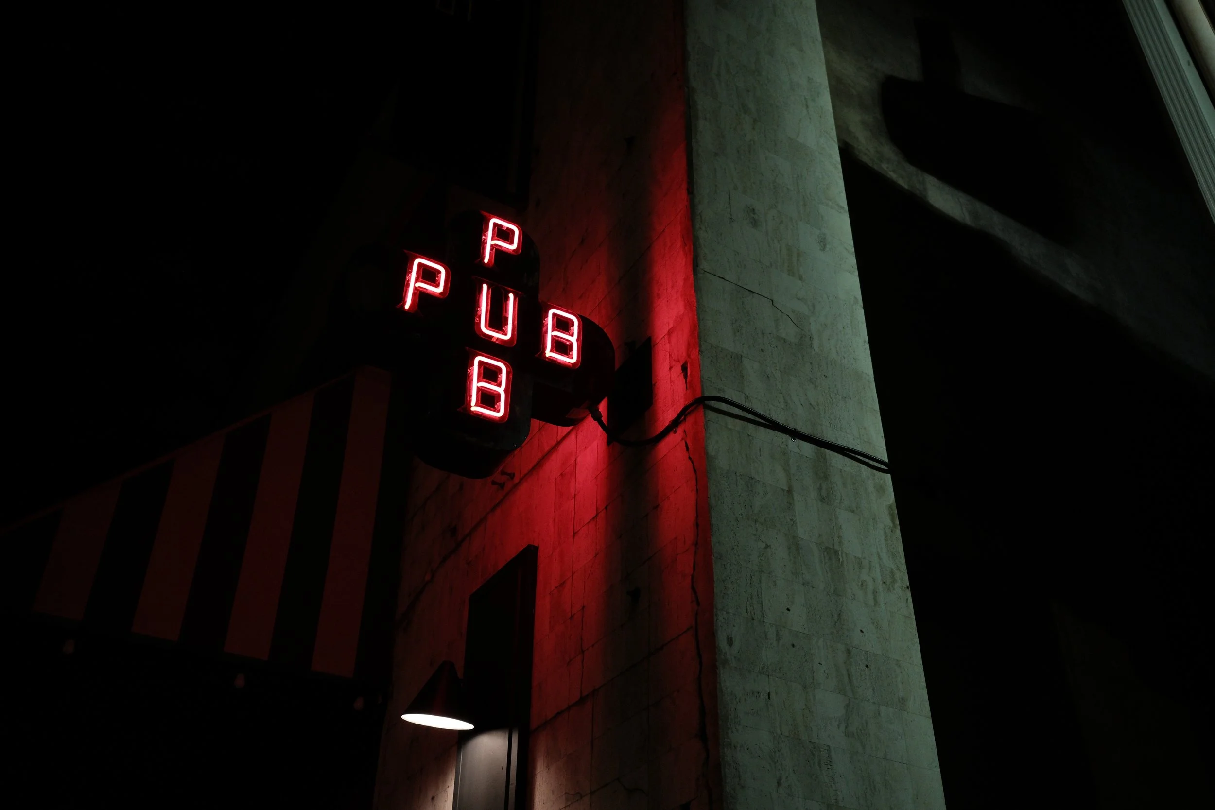 Red neon sign reading 'PUB' attached to a stone wall, with a small light illuminating the lower part of the scene at night.