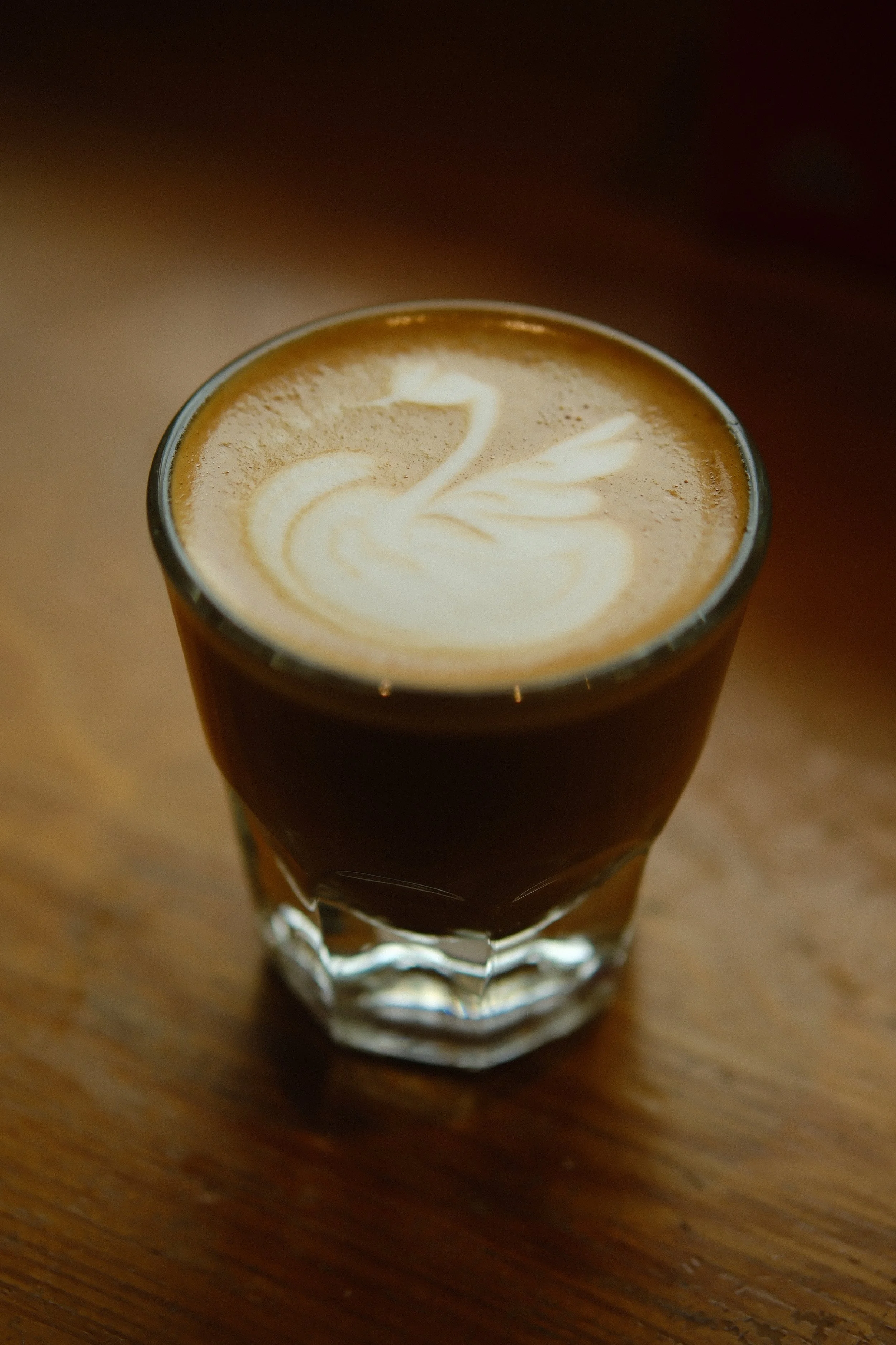 A glass of coffee with latte art in the shape of a swan on top.