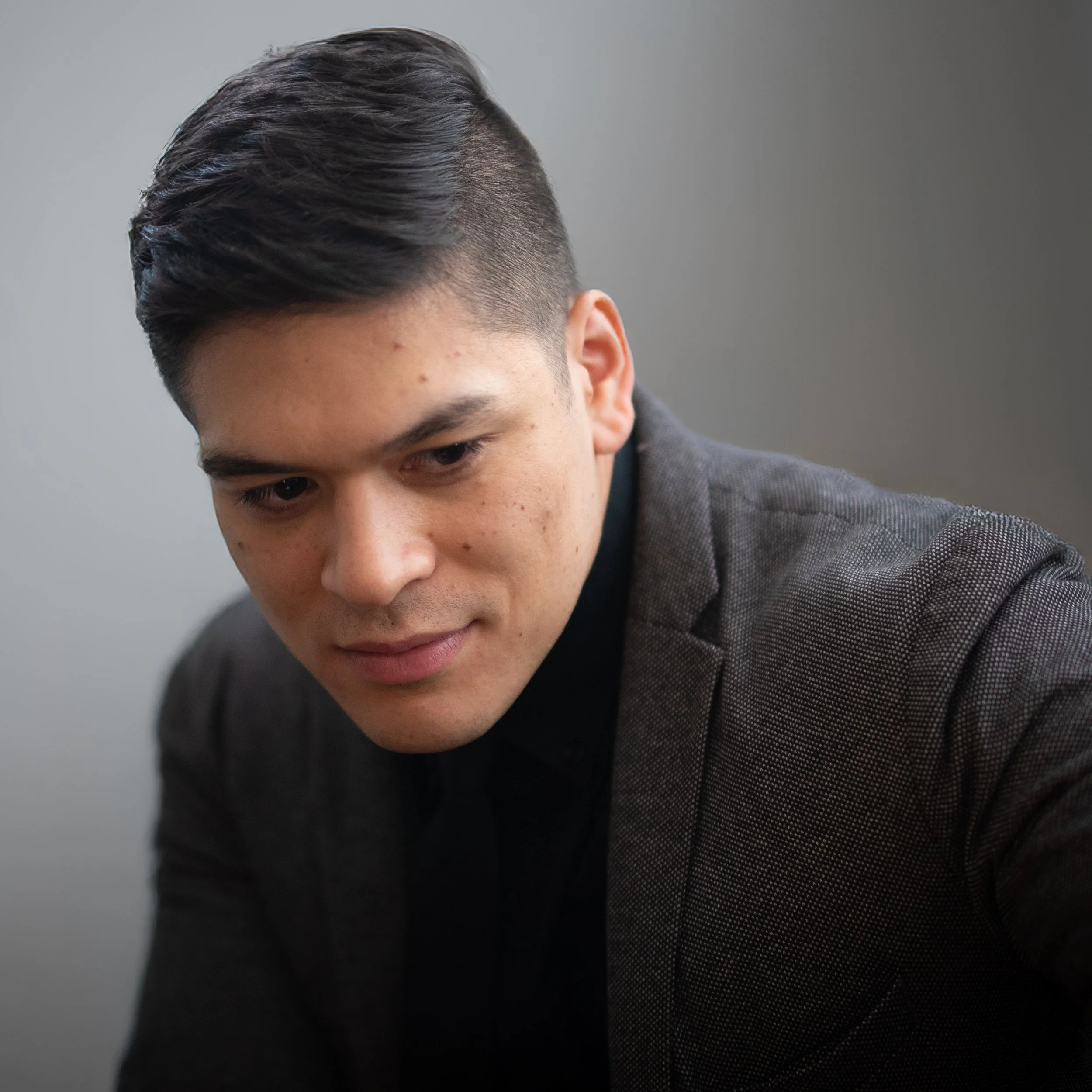Man in a gray suit looking down with a neutral expression
