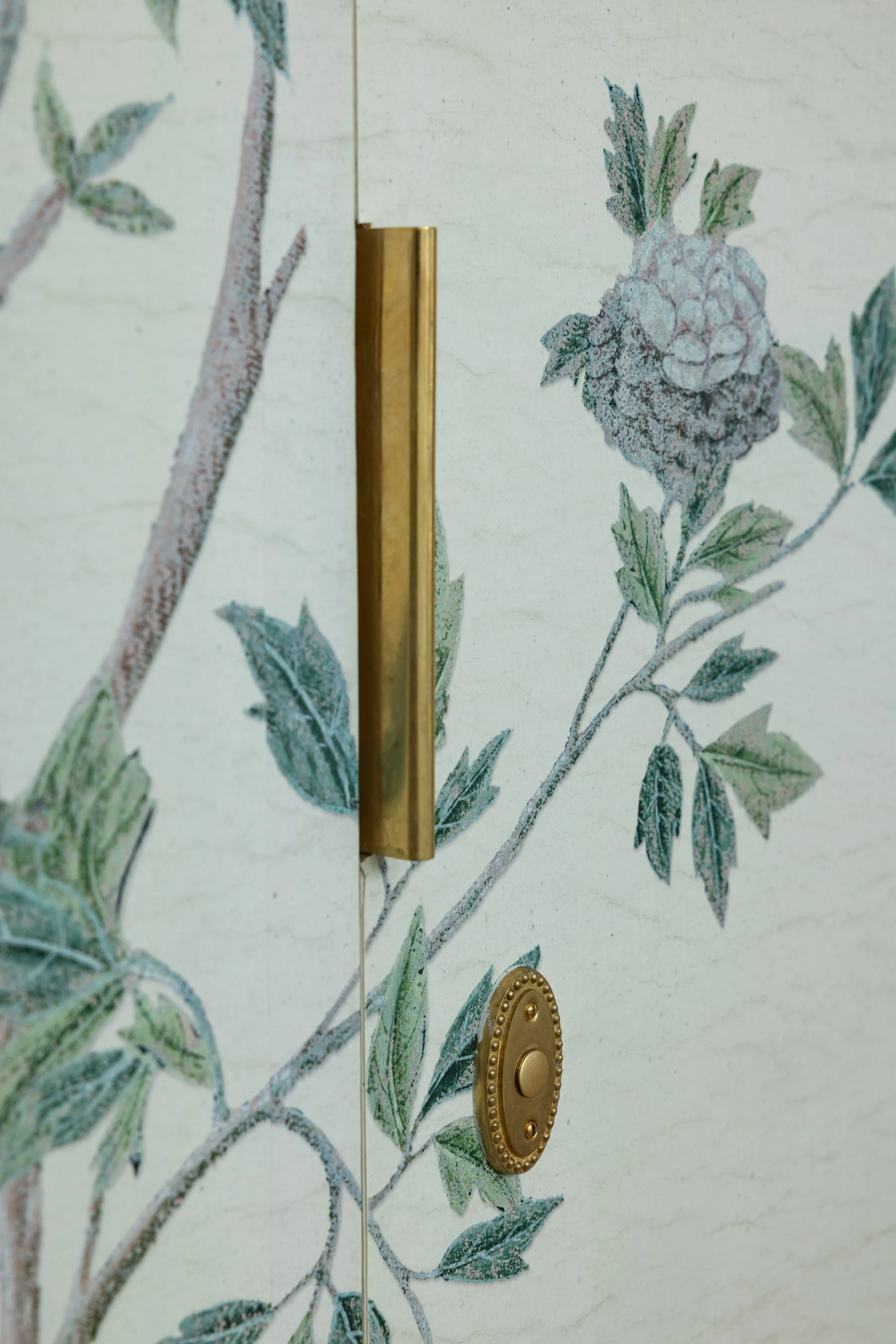 Close-up of a door with a brass handle and a brass lock, decorated with a floral and berry pattern.