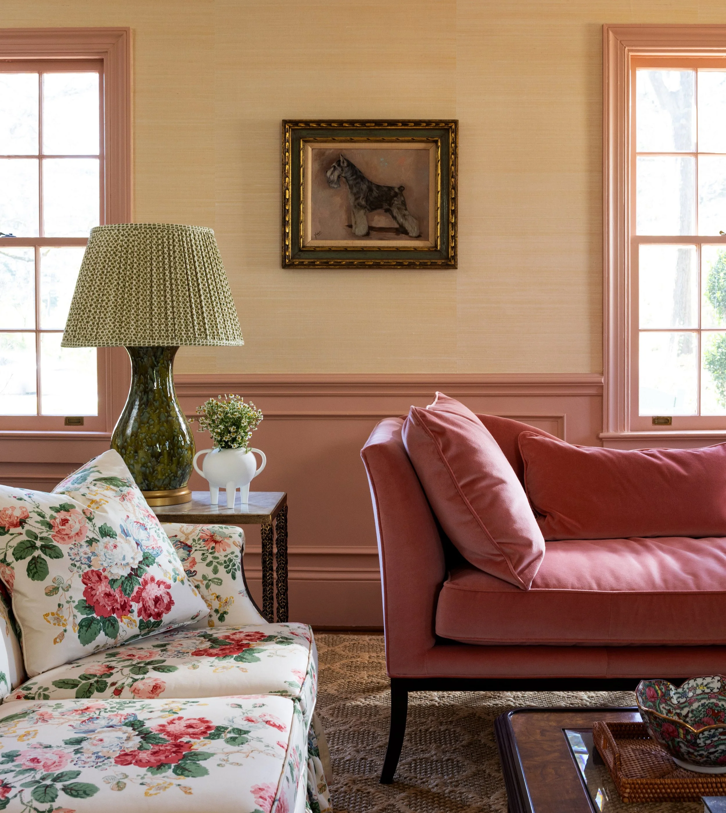 Living room with pink sofa, floral armchair, table lamp, framed horse painting, large windows