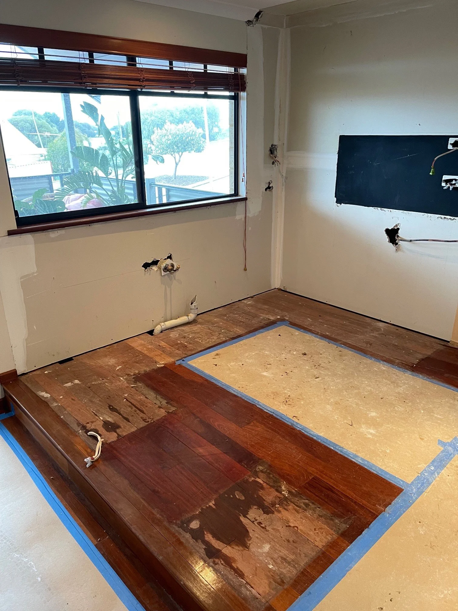 Room under renovation with partially replaced wooden floor and window with blinds.