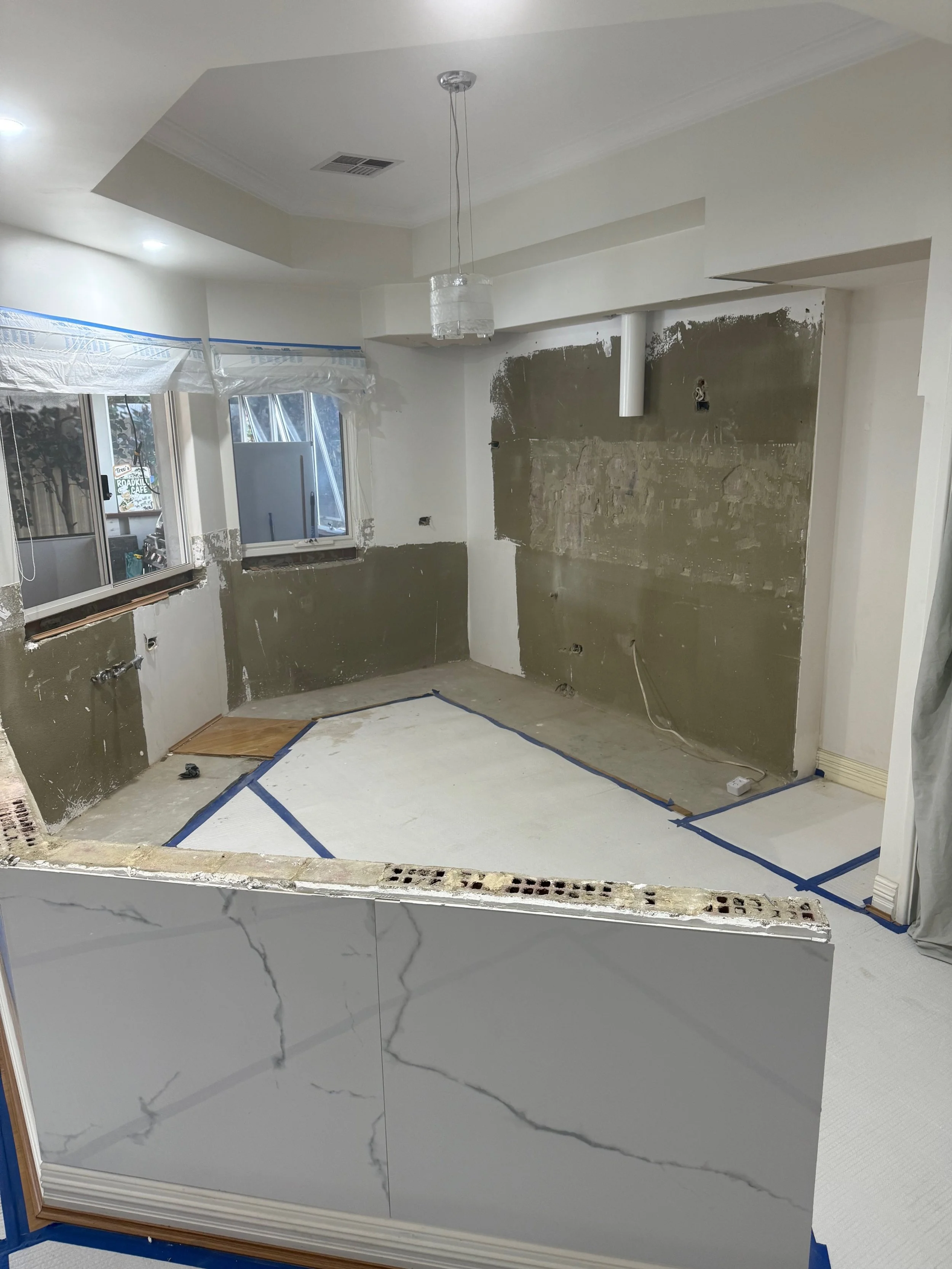 Kitchen renovation in progress with partially removed cabinets, drywall work underway, and construction materials visible.