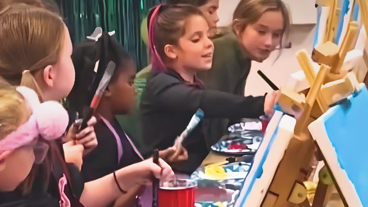 Children gathered around an art station painting and drawing on canvases
