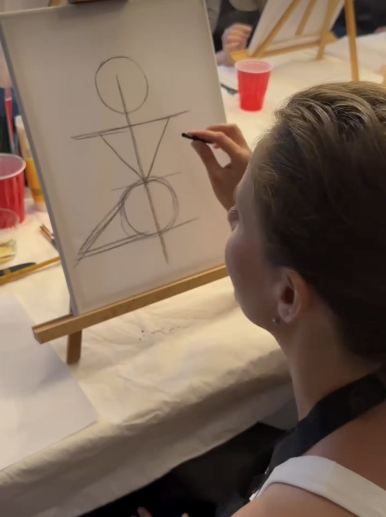 A person drawing geometric shapes and lines on a whiteboard as part of an art or design activity.