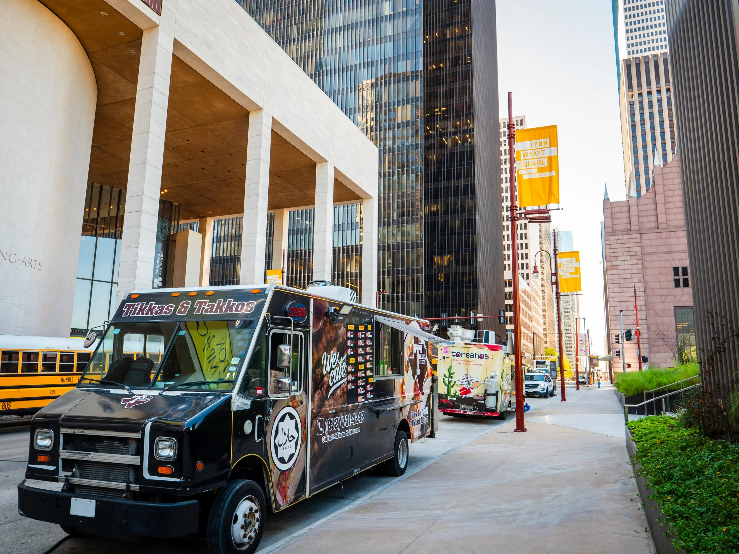 City street scene with food trucks in front of Jones Hall. One food truck prominently features the name 'Tikkas & Takkos'.