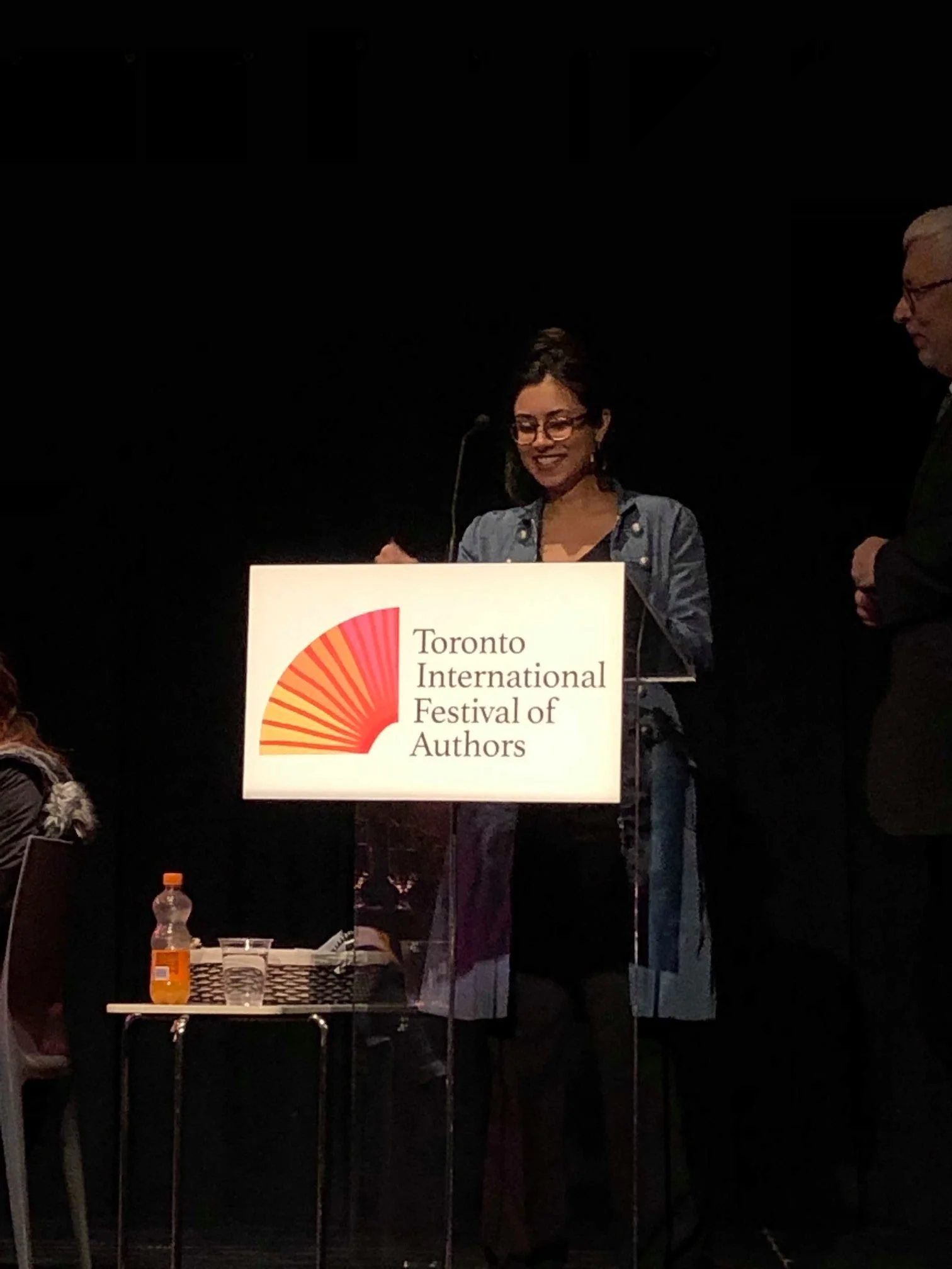 Woman speaking at a podium with a sign that reads 'Toronto International Festival of Authors'.