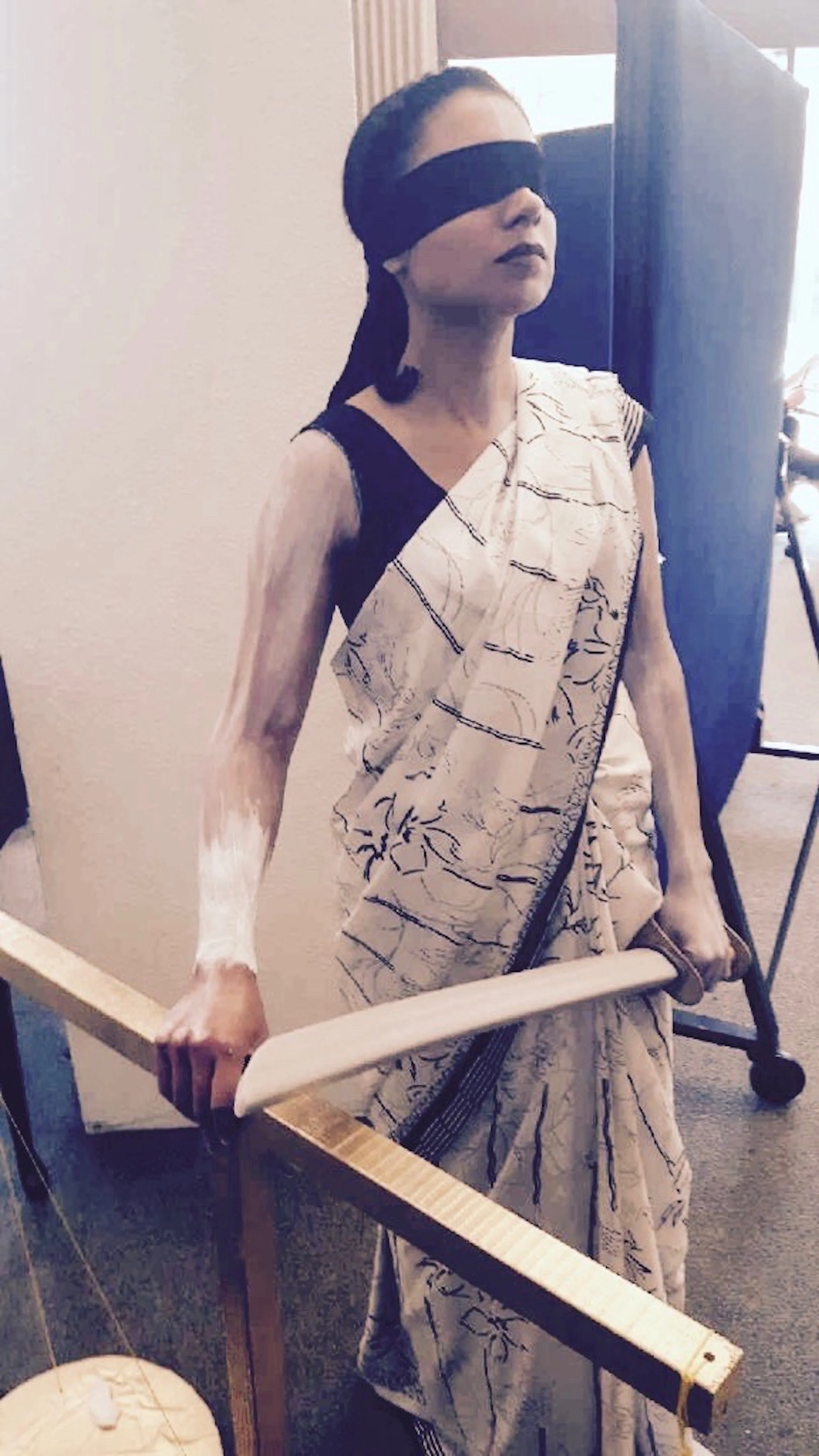 Preeti Kaur Dhaliwal in a saree blindfolded, holding a balance scale in her right hand and a wooden stick in her left hand.