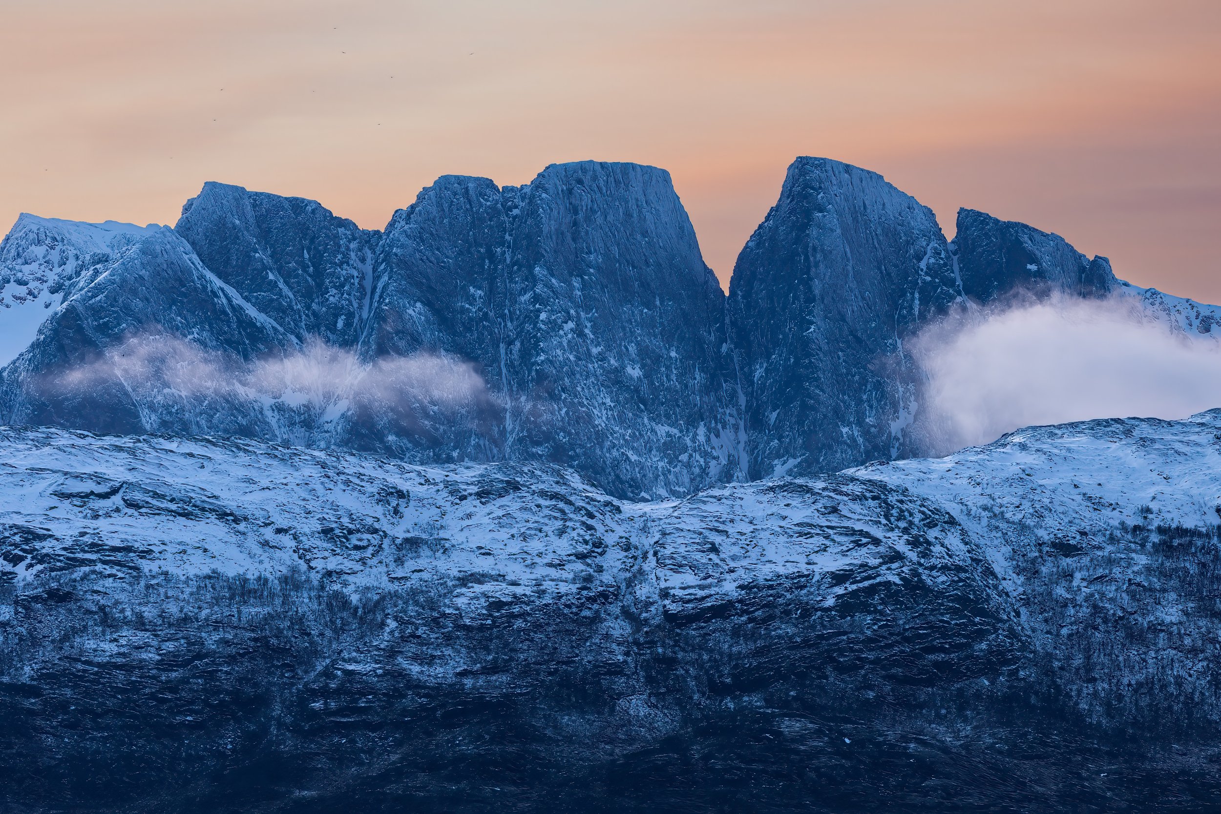 Snow-covered mountain range with clouds and orange sky
